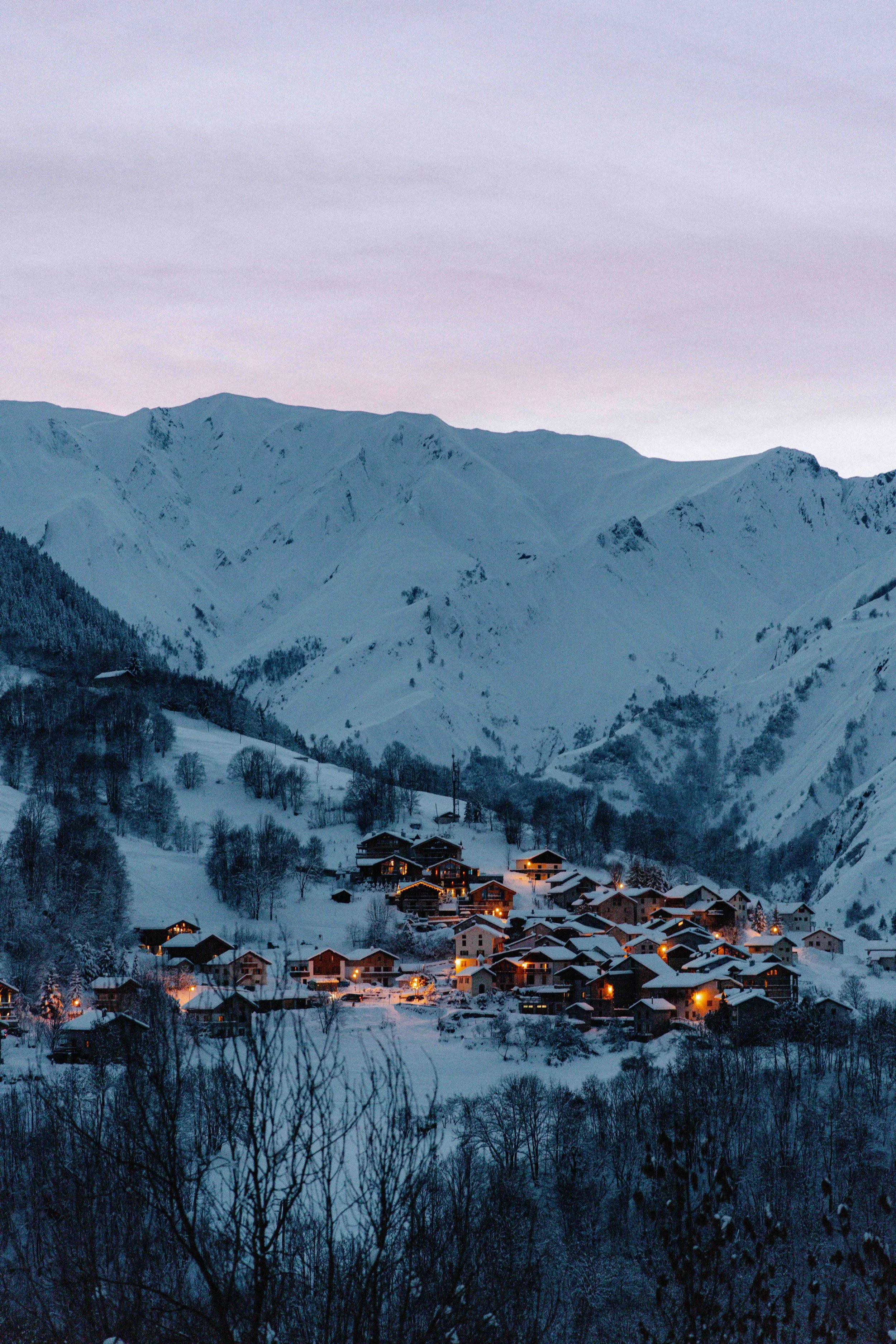 Snow-covered mountains and a small village with lit houses at dusk.