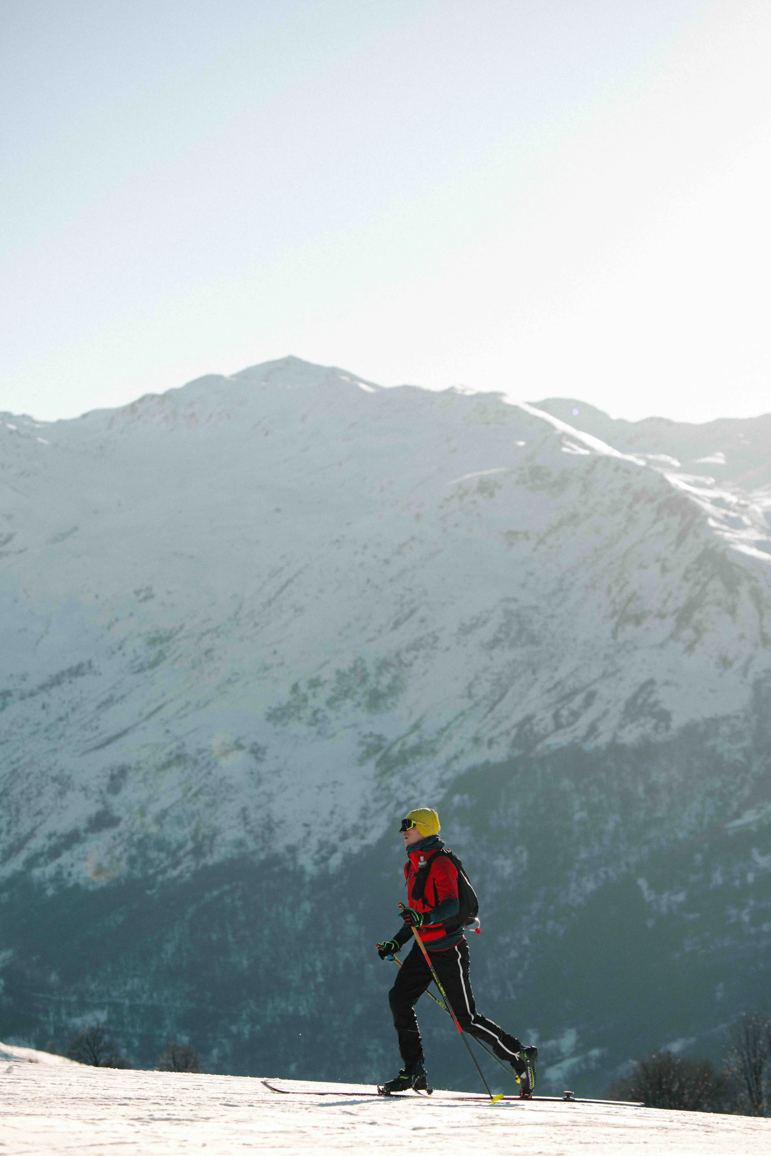 A person in winter gear skiing on a snow-covered slope with snow-capped mountains in the background.