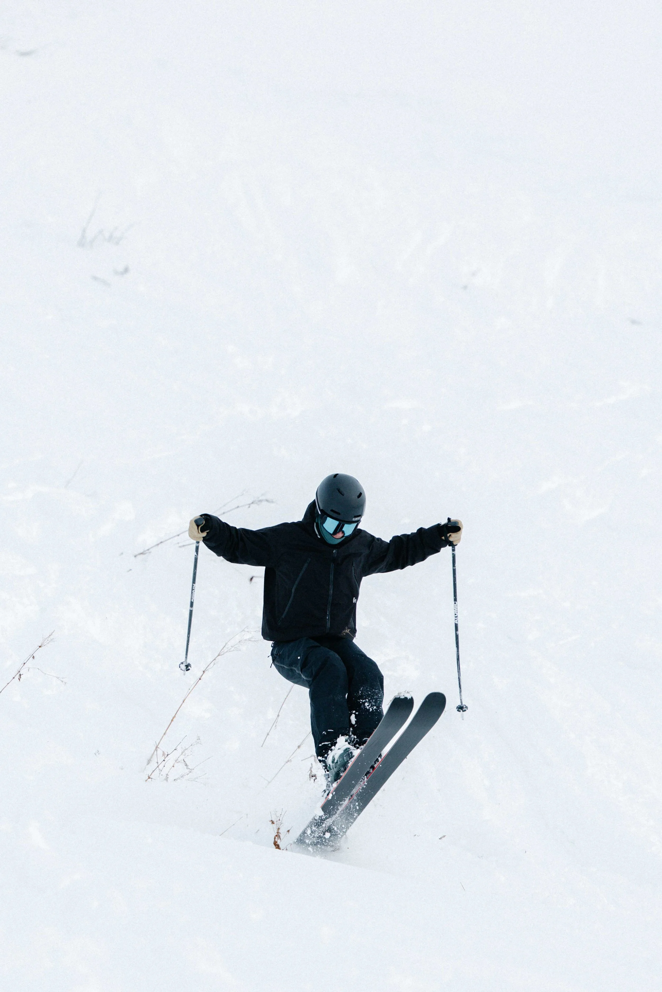 Person wearing black ski gear, helmet, and goggles skiing down a snowy slope.