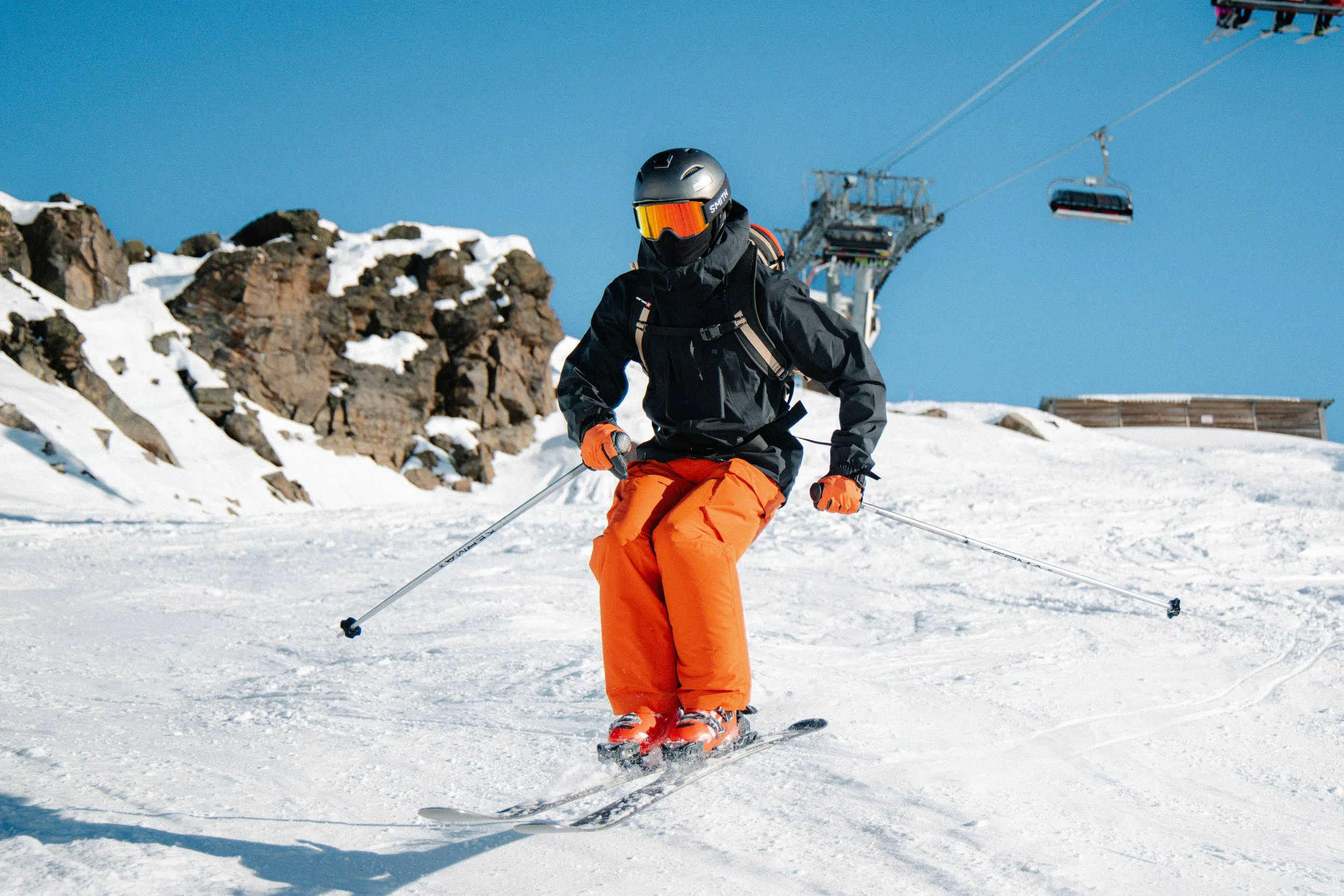 A person skiing on snow-covered slopes with rocks and a ski lift in the background.