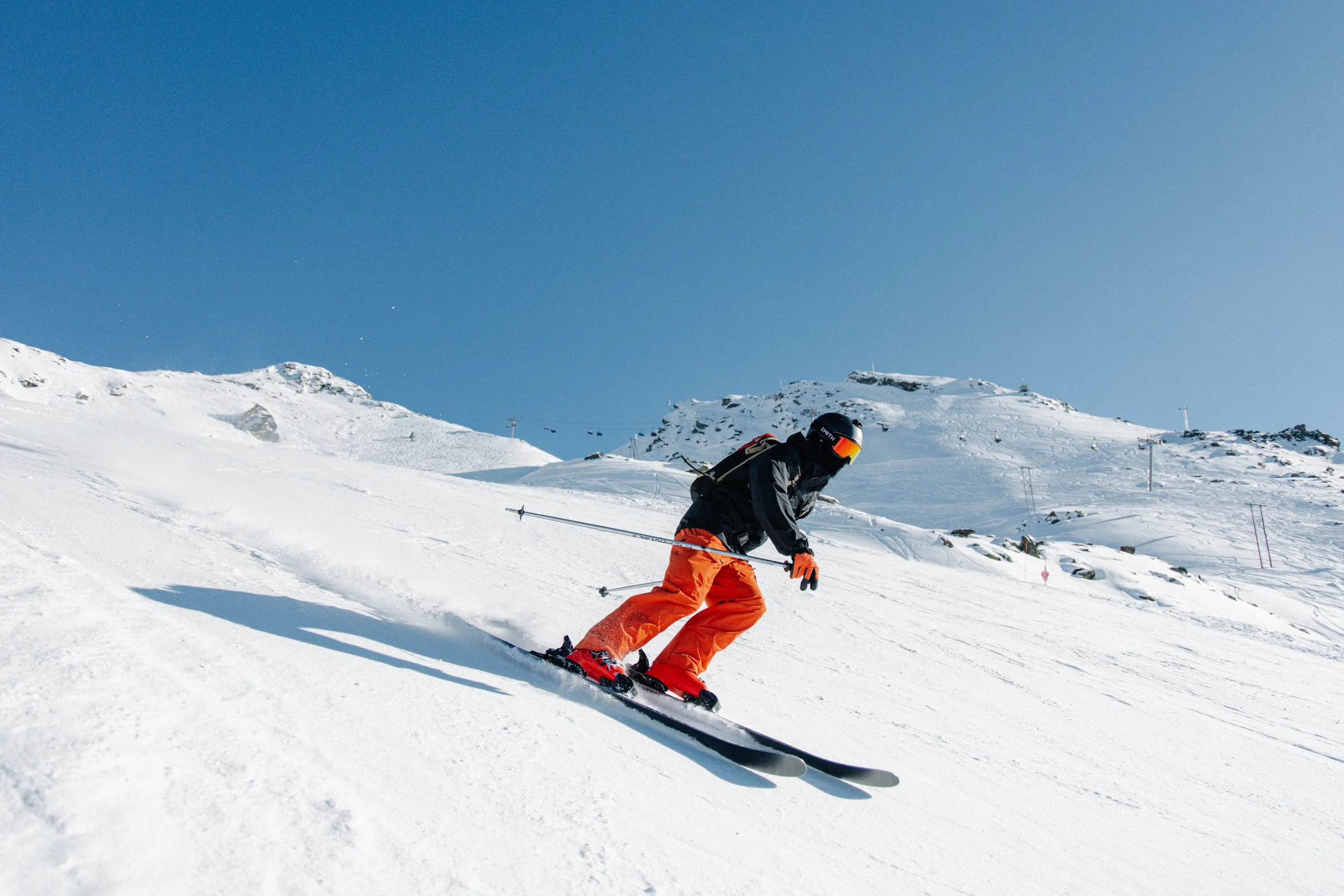 A person skiing down a snowy slope on a clear winter day, wearing an orange jacket and black helmet.