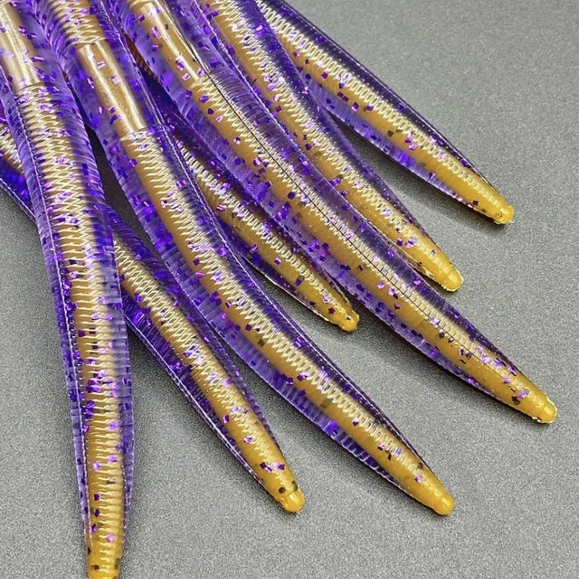 Close-up of the Chaney Creek 5-inch Futoi (Senko) core-shot fishing worms with translucent purple bodies, bright yellow cores, and glitter flakes.