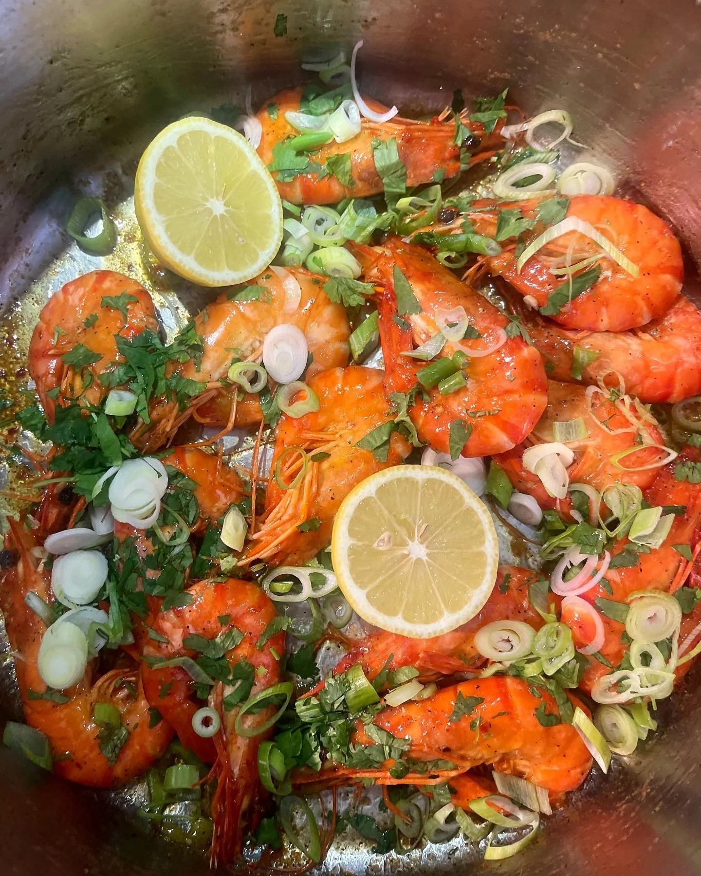 Cooked shrimp garnished with lemon slices, chopped green onions, and herbs.