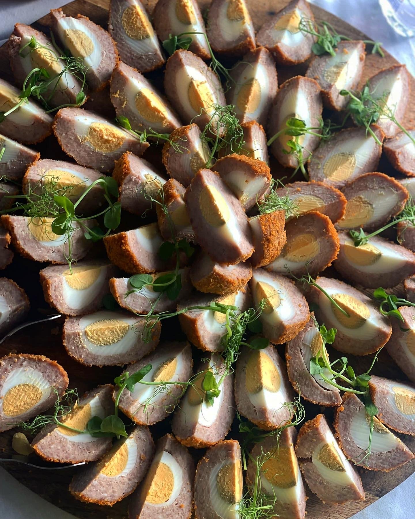 A platter of sliced Scotch eggs garnished with microgreens.
