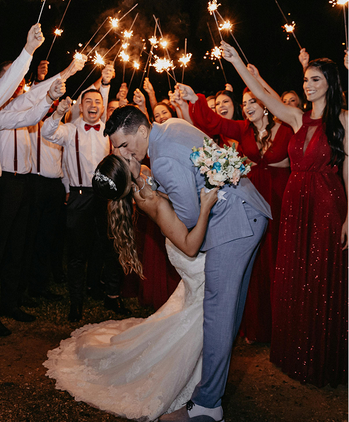 Bride and groom kissing during their wedding reception at night, surrounded by wedding guests holding sparklers and celebrating.