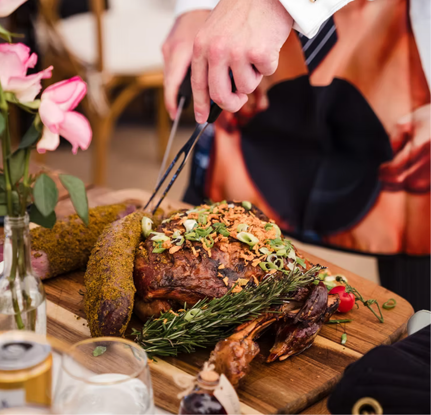 Person carving a roasted holiday turkey garnished with herbs and vegetables on a wooden cutting board.