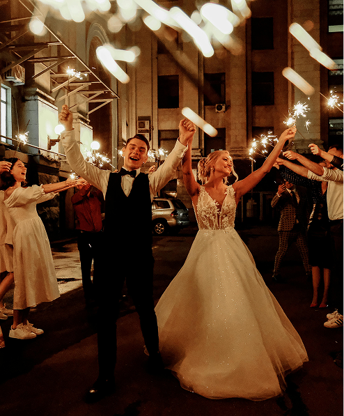 Bride and groom celebrating with sparklers at night, surrounded by friends.