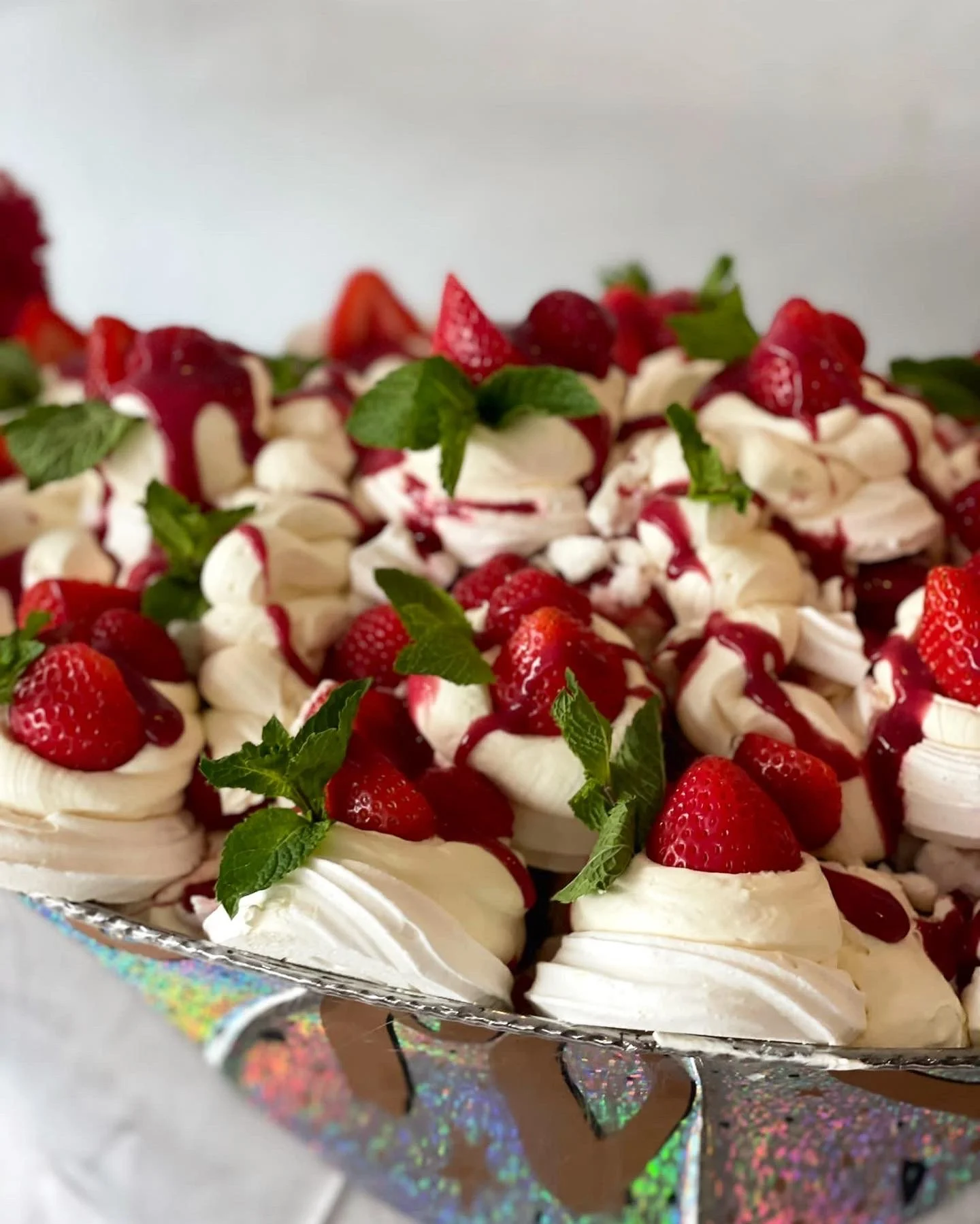 A dessert tray filled with whipped cream, fresh strawberries, and mint leaves, drizzled with red sauce.