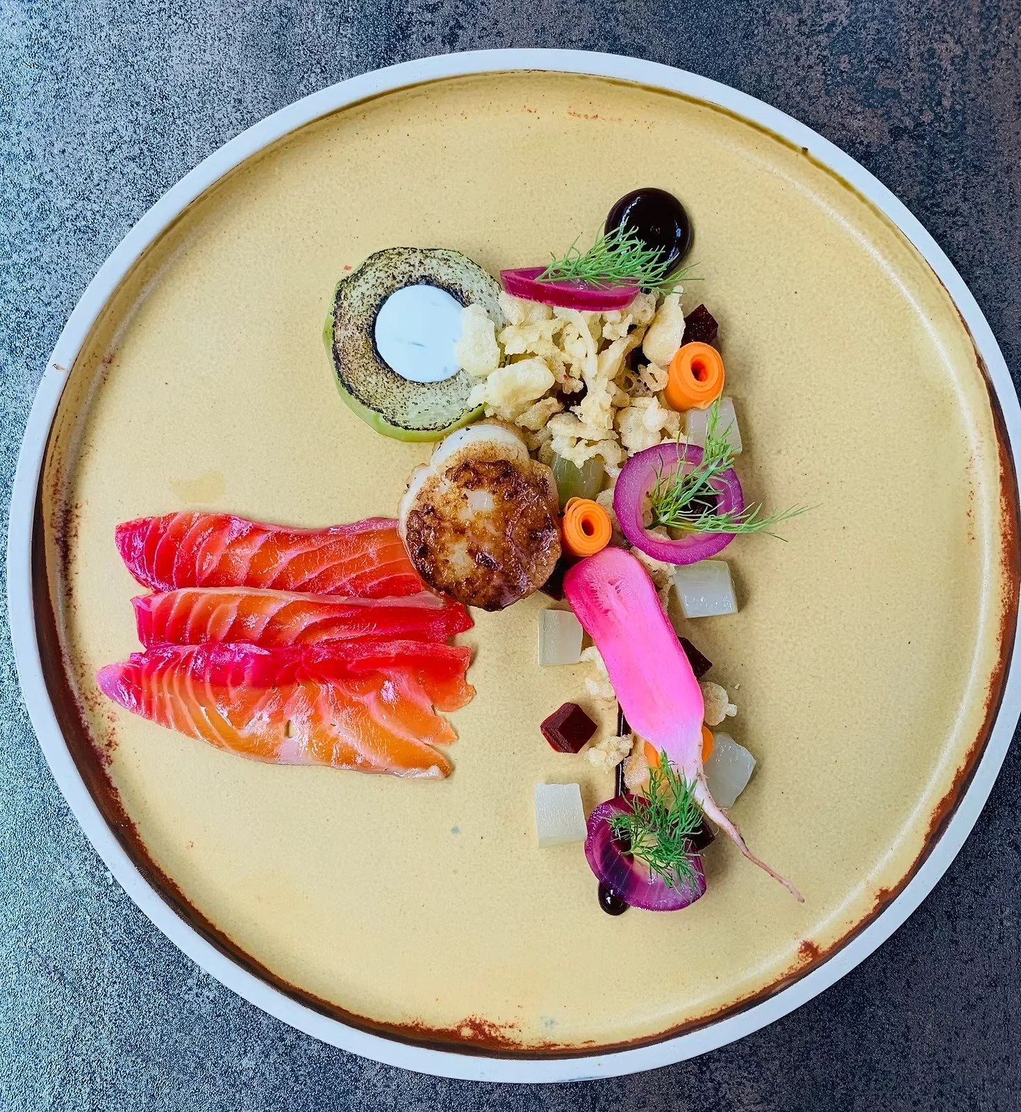A plate of assorted colorful appetizers, including smoked salmon, sliced cucumber with a filling, diced vegetables, and garnishes, on a white dish.