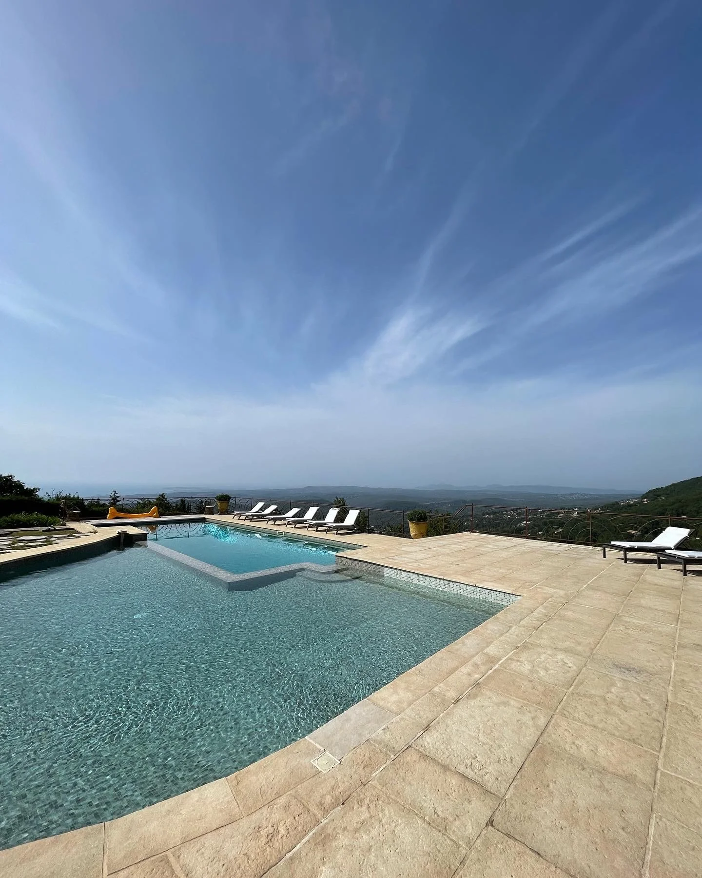 Luxury outdoor swimming pool with lounge chairs and a scenic view of hills and sky.