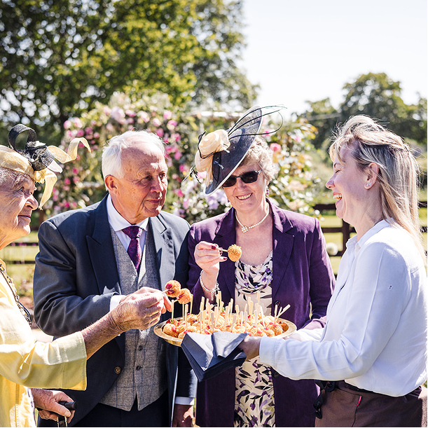Group of elderly people celebrating outdoors, with a woman holding a tray of appetizers or cake with candles, and others enjoying the moment