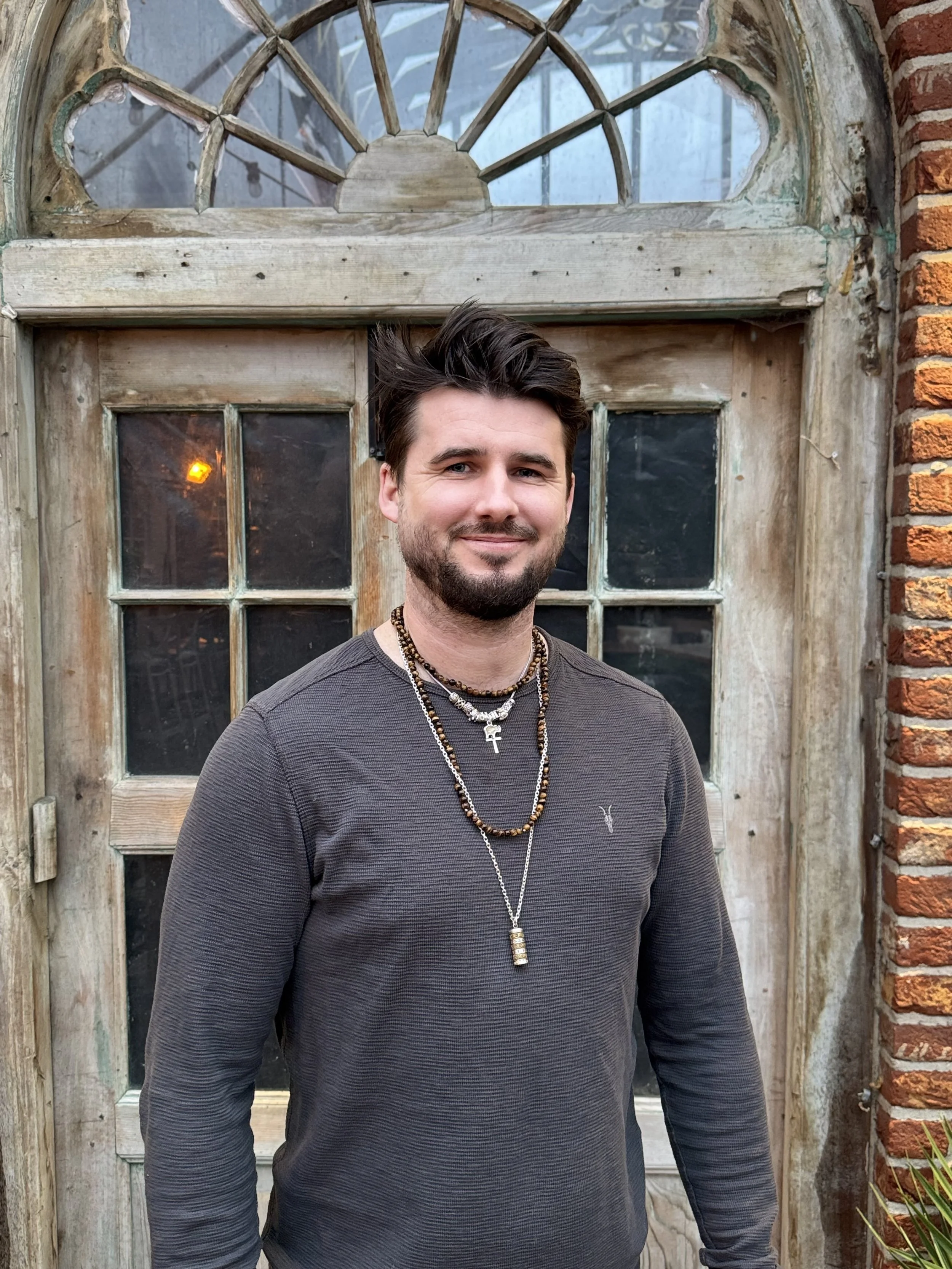 A middle-aged man with gray hair, wearing a blue short-sleeve sweater and beige pants, sits on a bench against a beige wall with a shadow cast behind him.