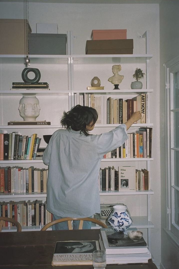 Une personne debout devant une étagère remplie de livres, qui semble atteindre pour en prendre un.