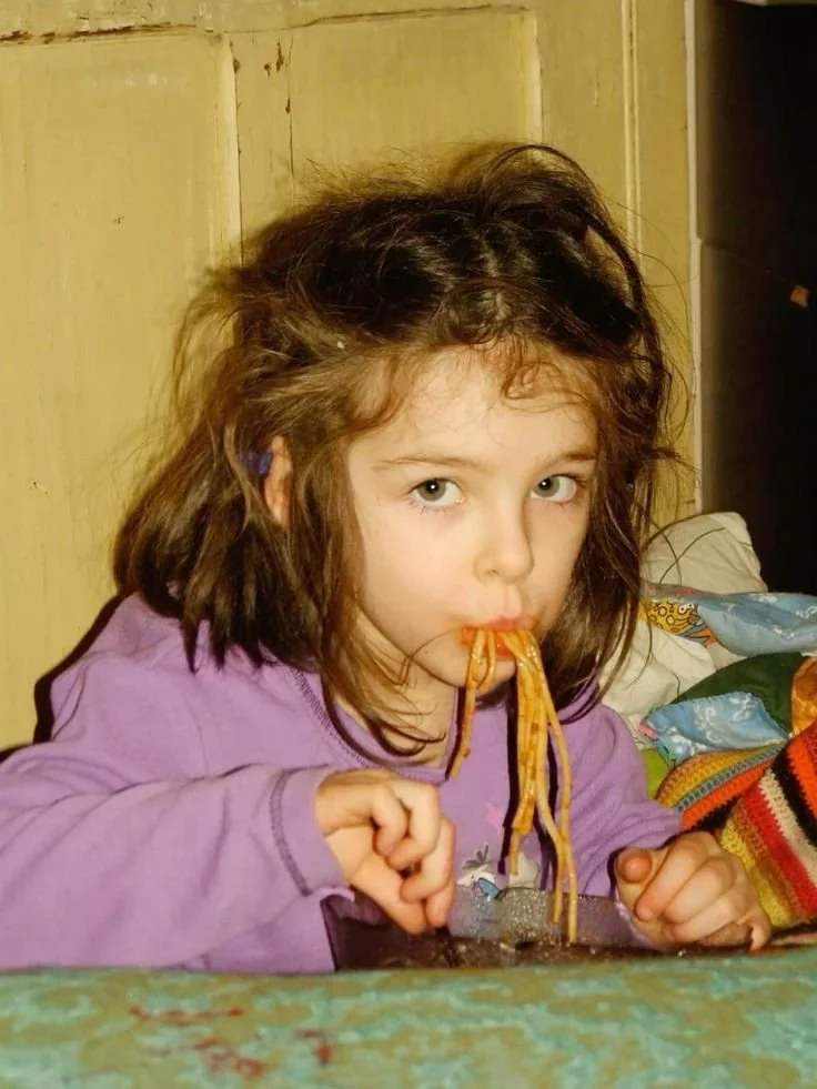 Une jeune fille avec des cheveux en désordre mange des nouilles dans un plat.