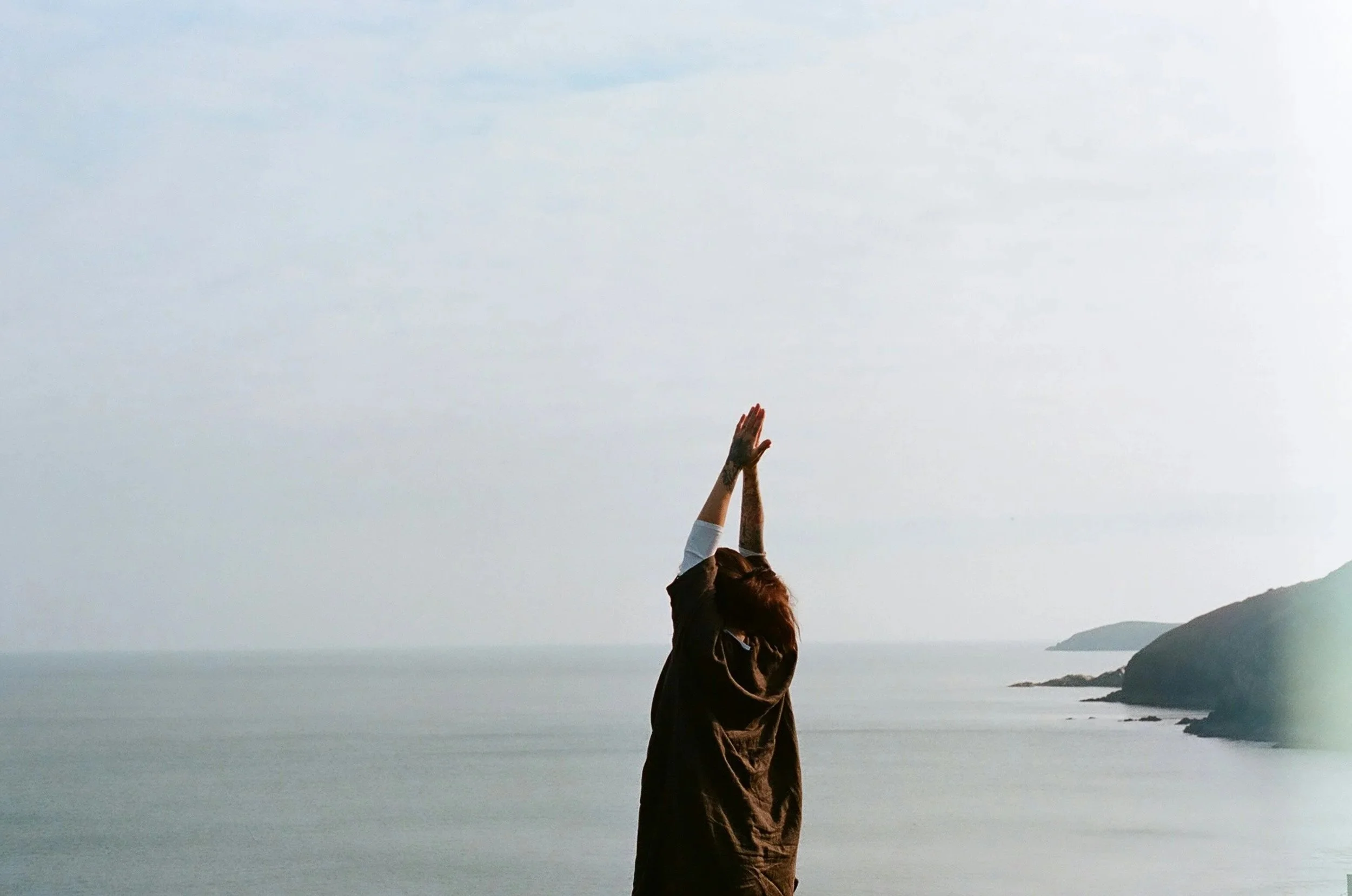 Una donna sta facendo stretching o meditazione di fronte al mare con le mani alzate sopra la testa.
