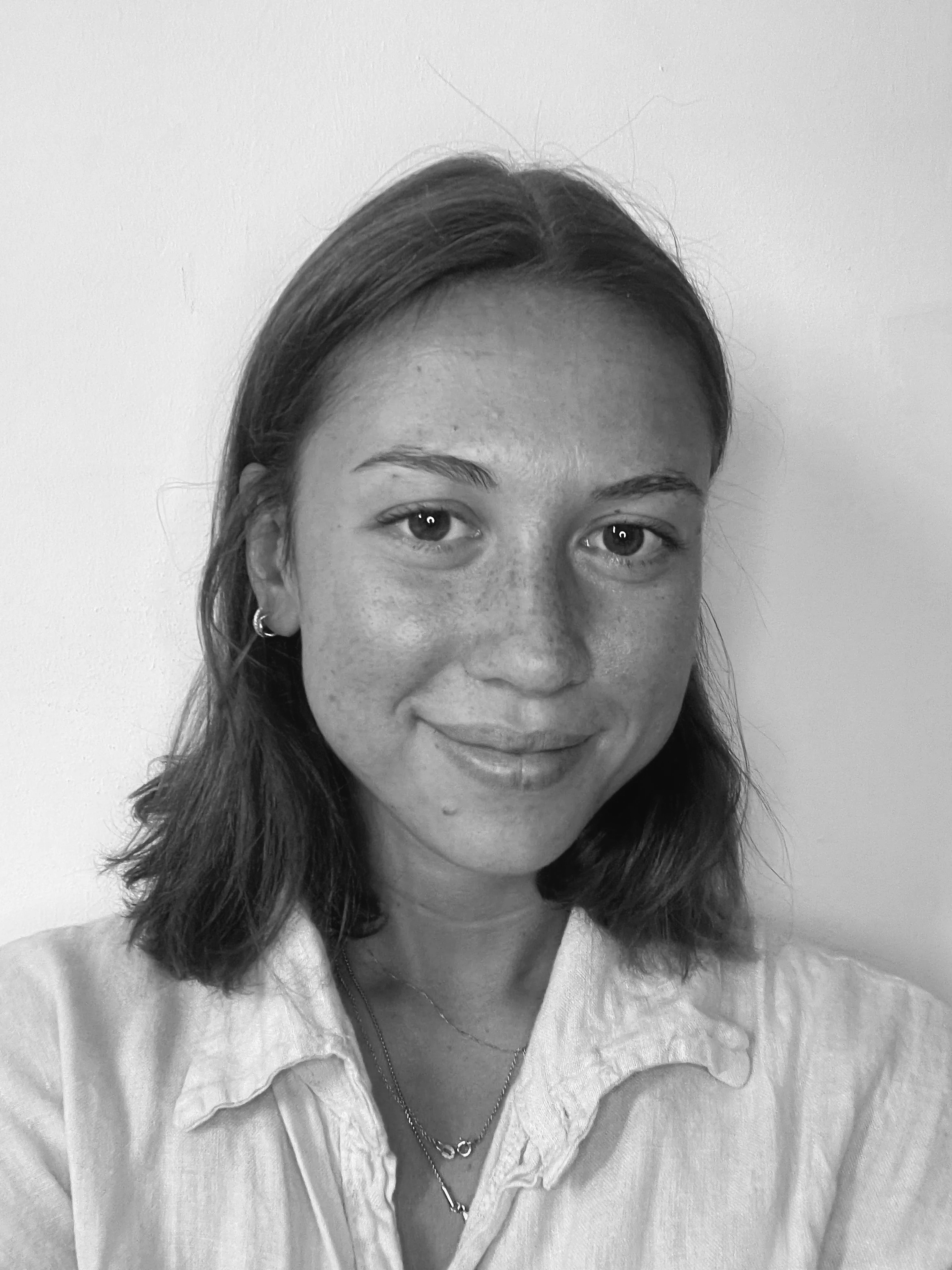 Ragazza sorridente con capelli castani, indossa una camicia chiara e gioielli, sfondo bianco.