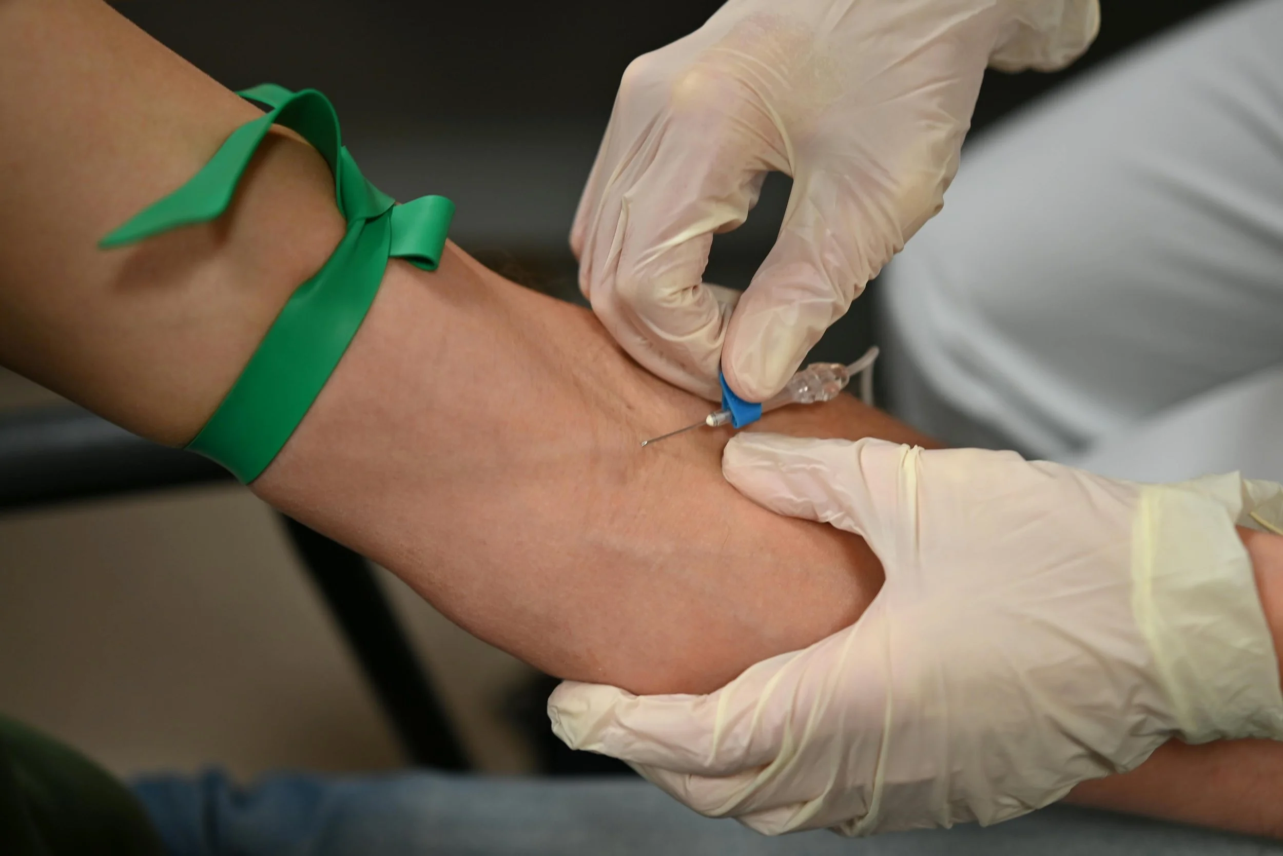 A person is receiving a blood draw from a healthcare professional. The healthcare worker is wearing white gloves and inserting a needle into the person's arm, PICC line, Midline, Peripherally inserted central line catheter