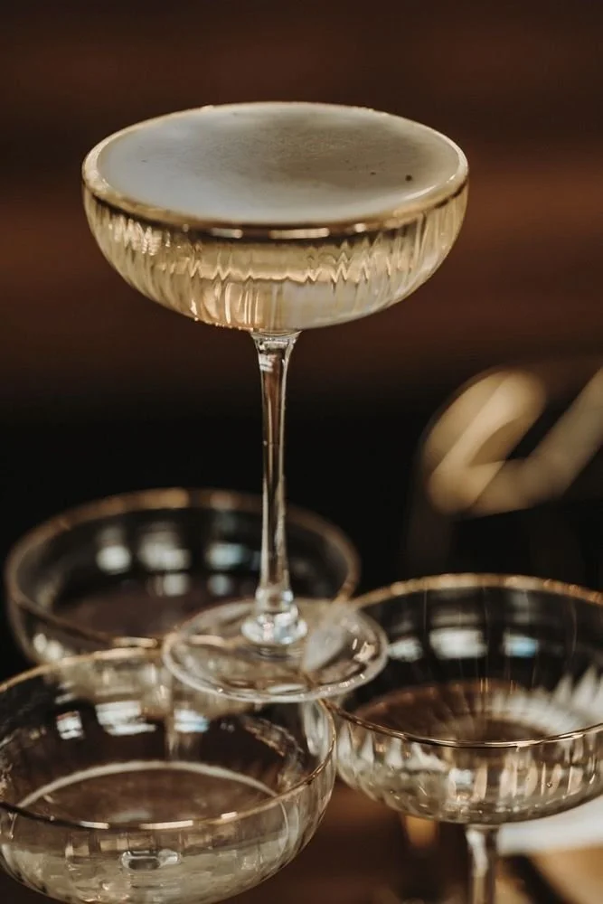 A glass of champagne balanced on top of two other coupe glasses, with a dark blurred background.