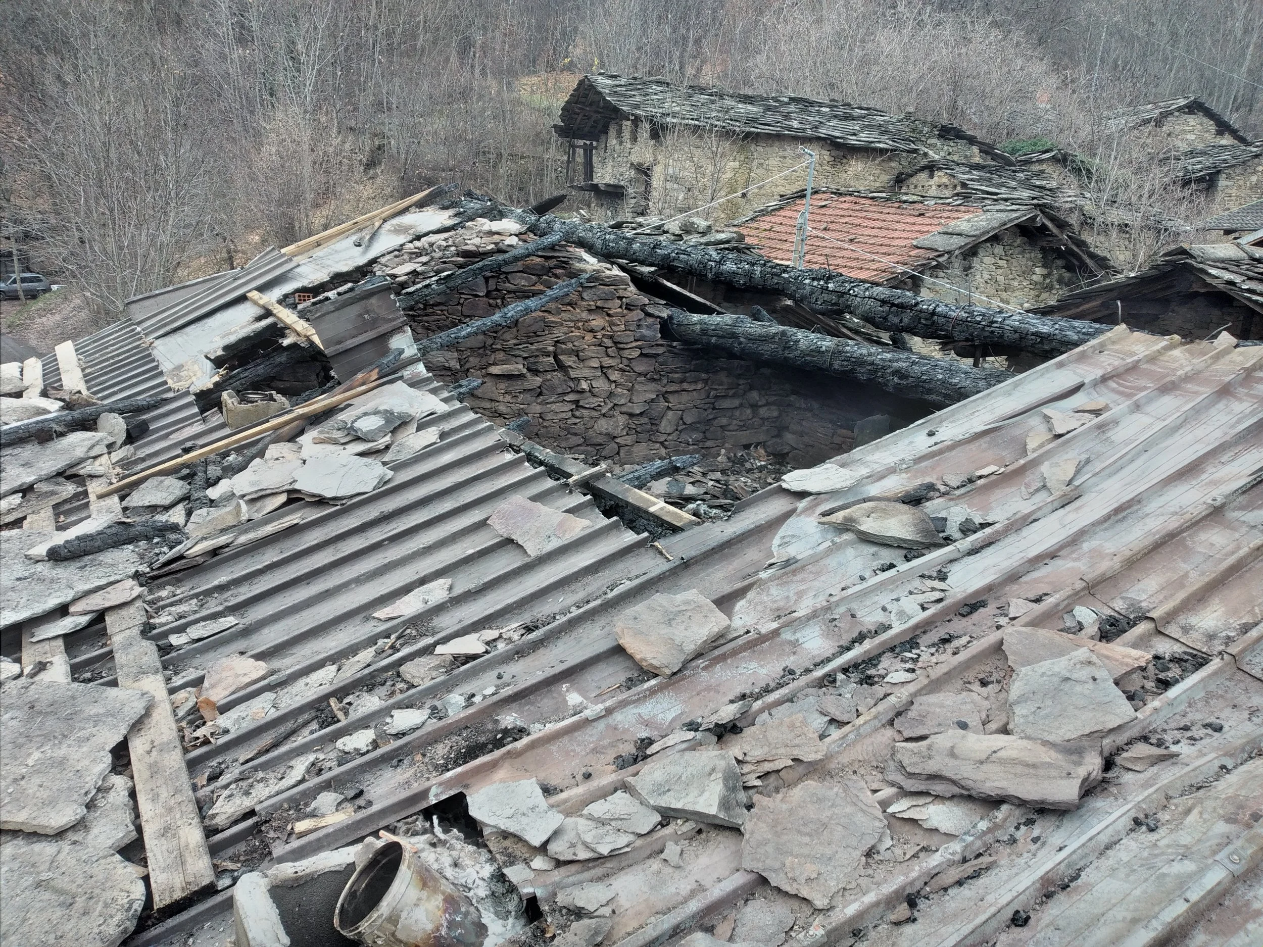 Tetto di una casa danneggiato da un incendio, con travi bruciate e tegole rotte.