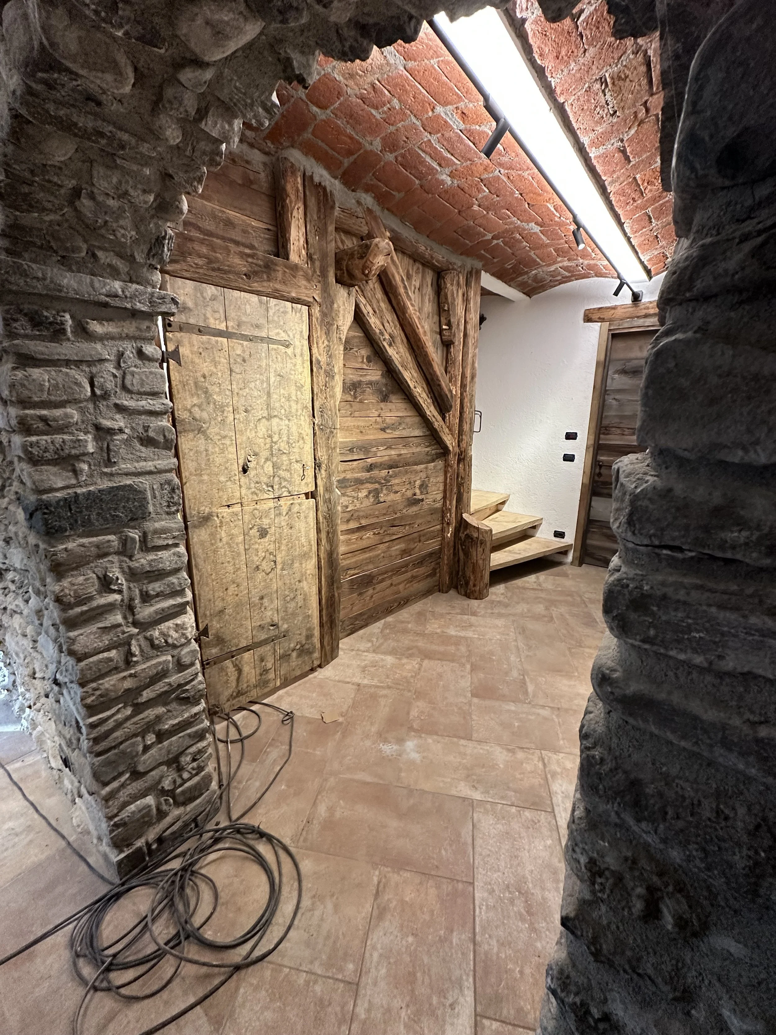 Interno in stile rustico con mattoni di tufo e pietra, con pareti in legno e scala in legno, illuminato da una luce LED attaccata al soffitto.