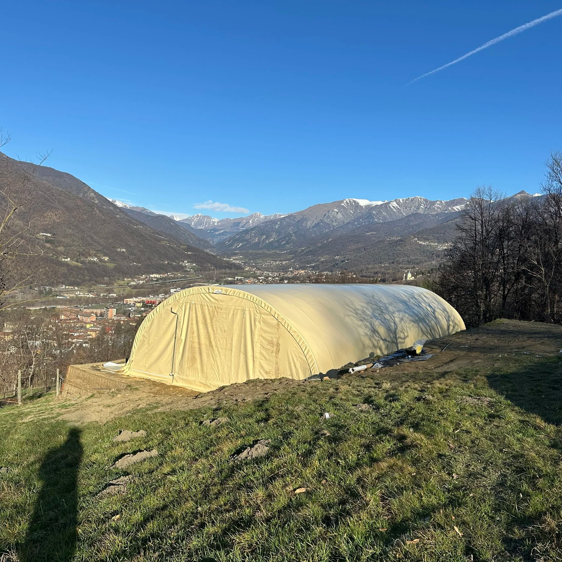 Tenda beige su un prato con una vista di montagne innevate sullo sfondo, cielo blu sereno.