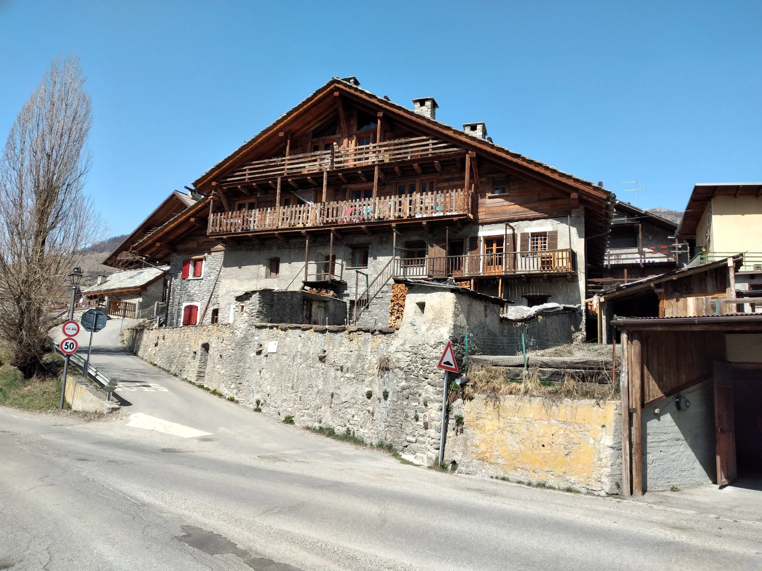 Casa in stile montano con grandi balconi di legno, strada ripida in primo piano, e alberi senza foglie ai lati