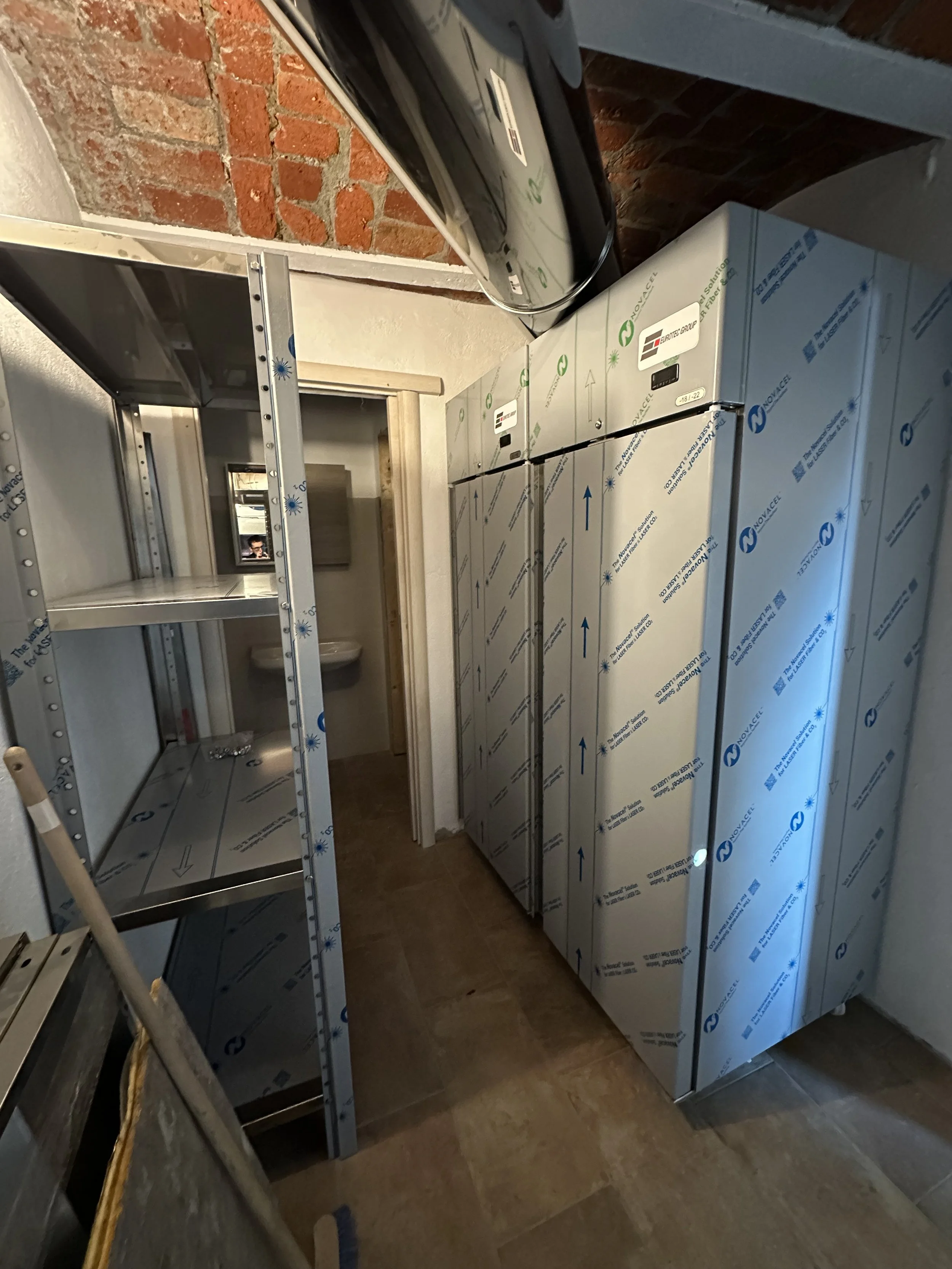 Stanza con armadi metallici di stoccaggio e scaffalature, senza persone, parete di mattoni e bagno visibile in stile rustico.