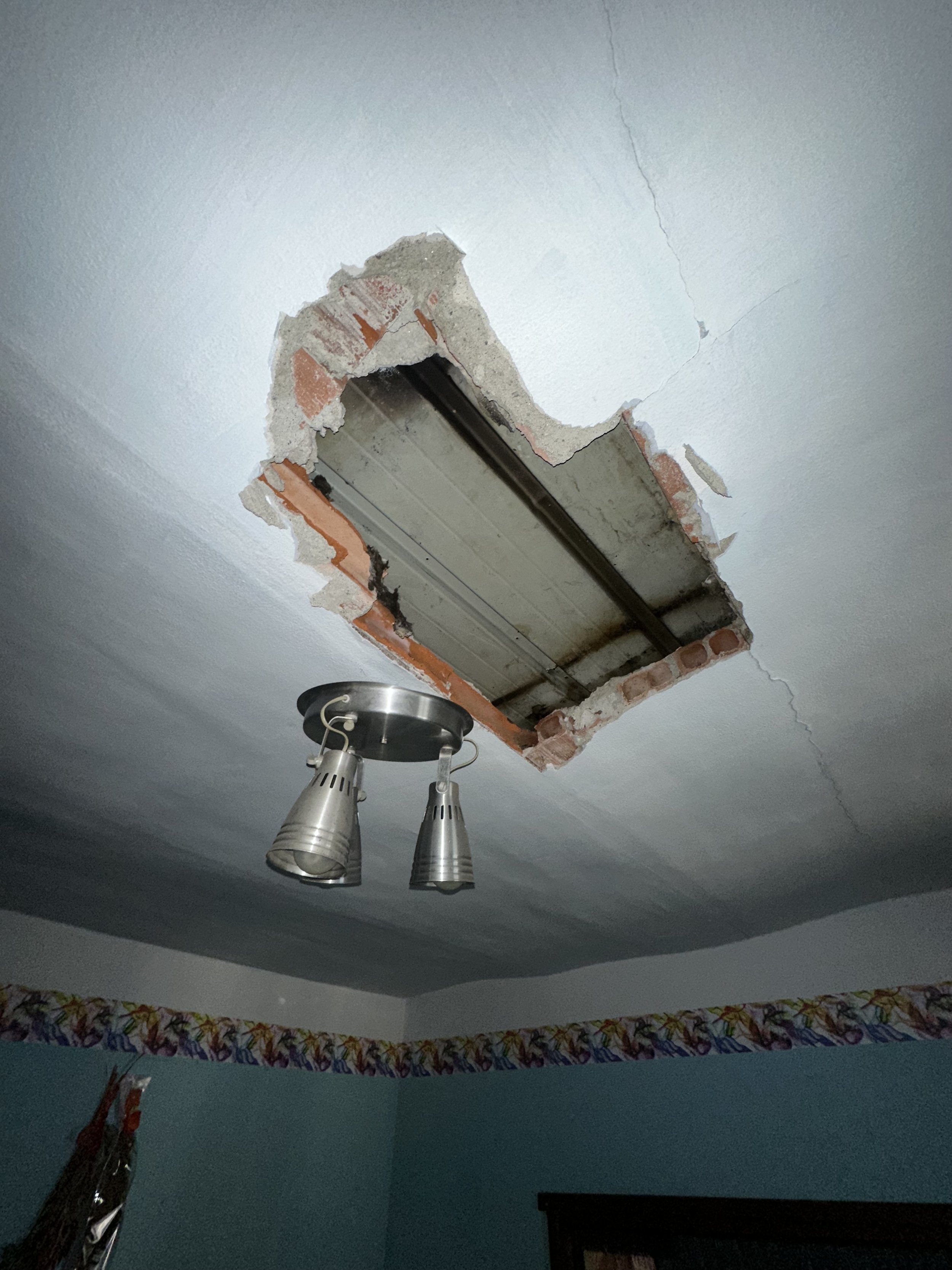 The ceiling has a large hole revealing the structure underneath, with a light fixture hanging from the ceiling.