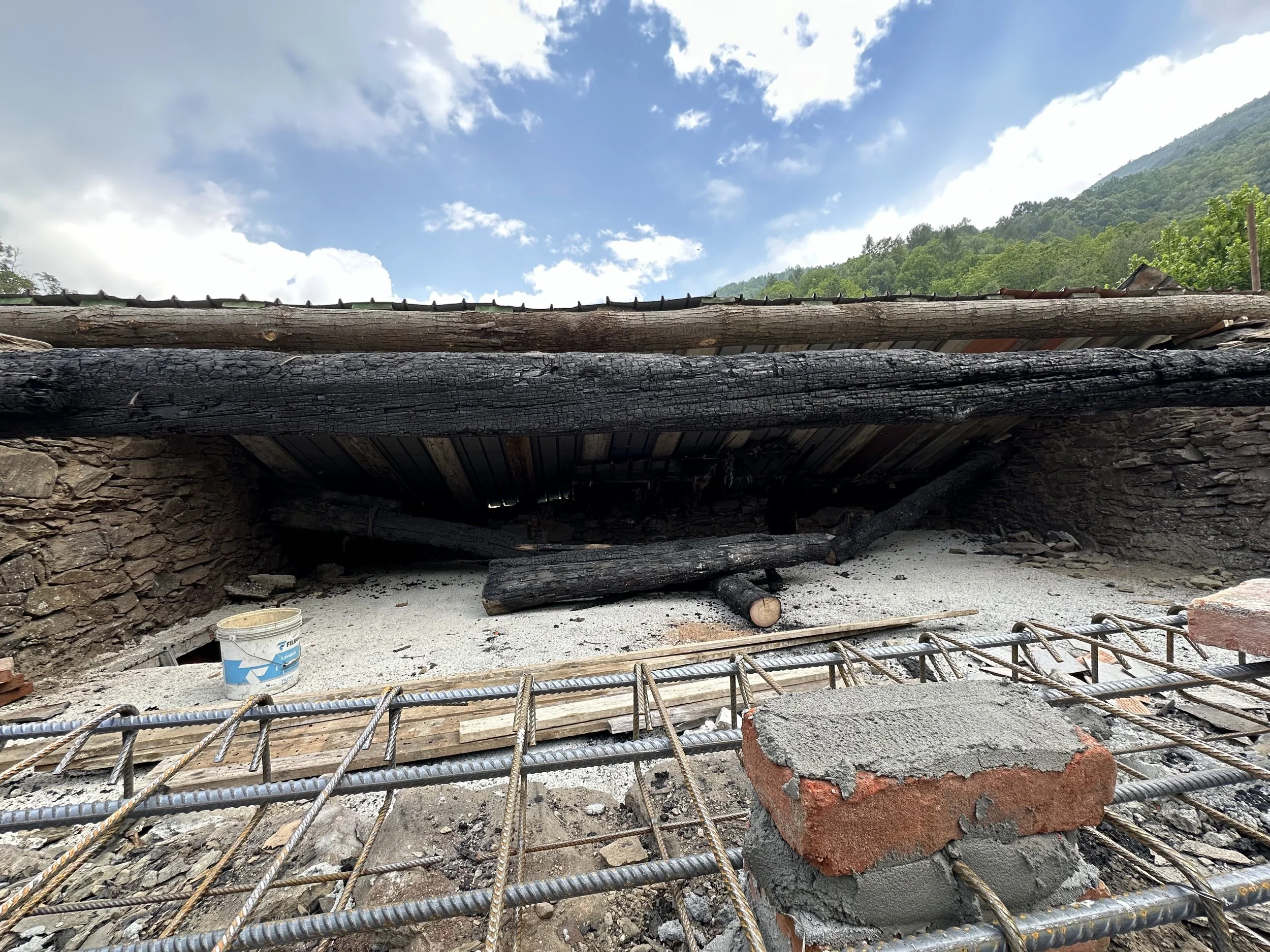 Struttura di un forno o ciminiera in costruzione con travi di legno bruciate, mattoni e rete di ferro.