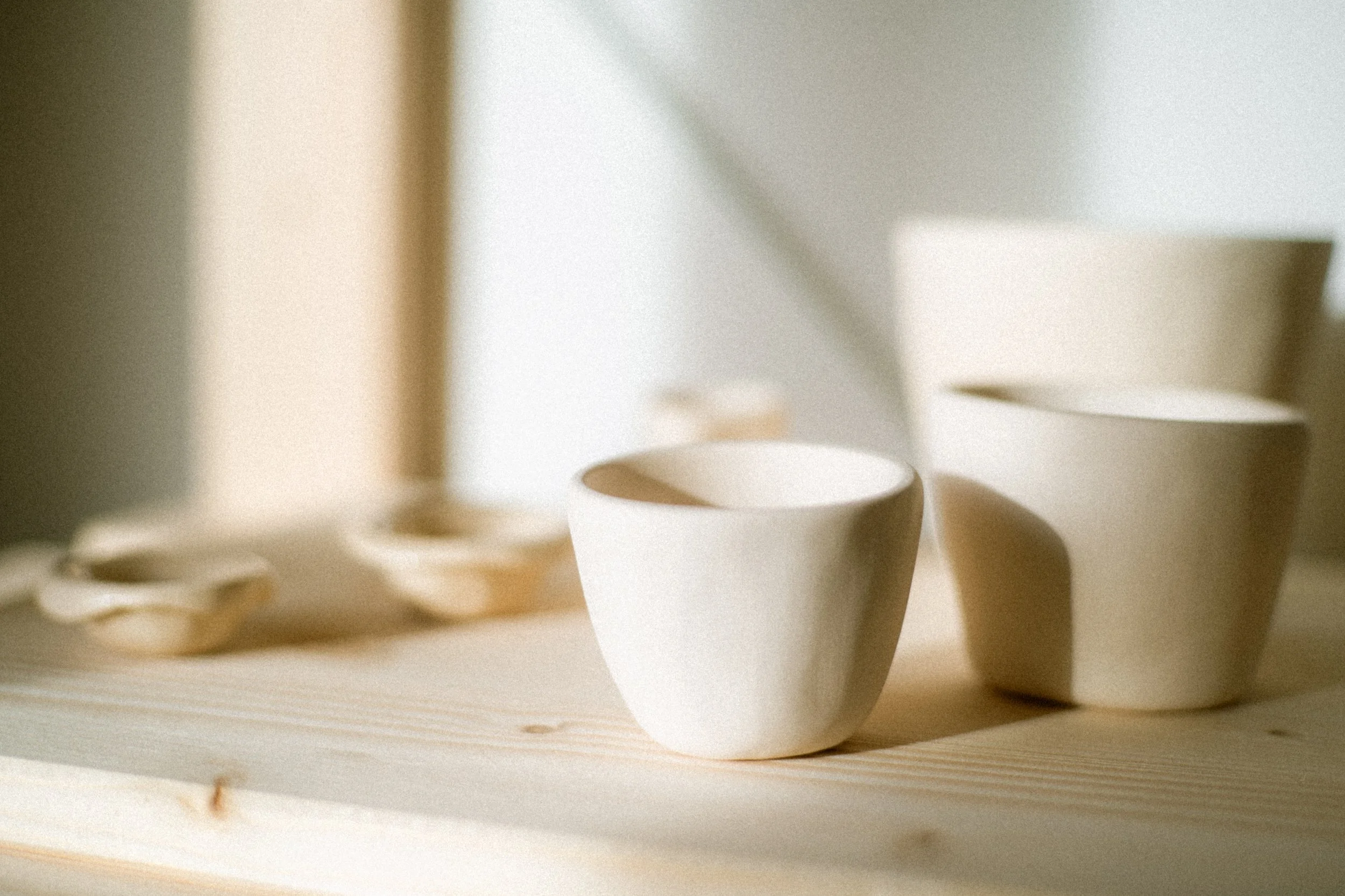 White ceramic cups and bowls on a light wooden surface, with soft natural light