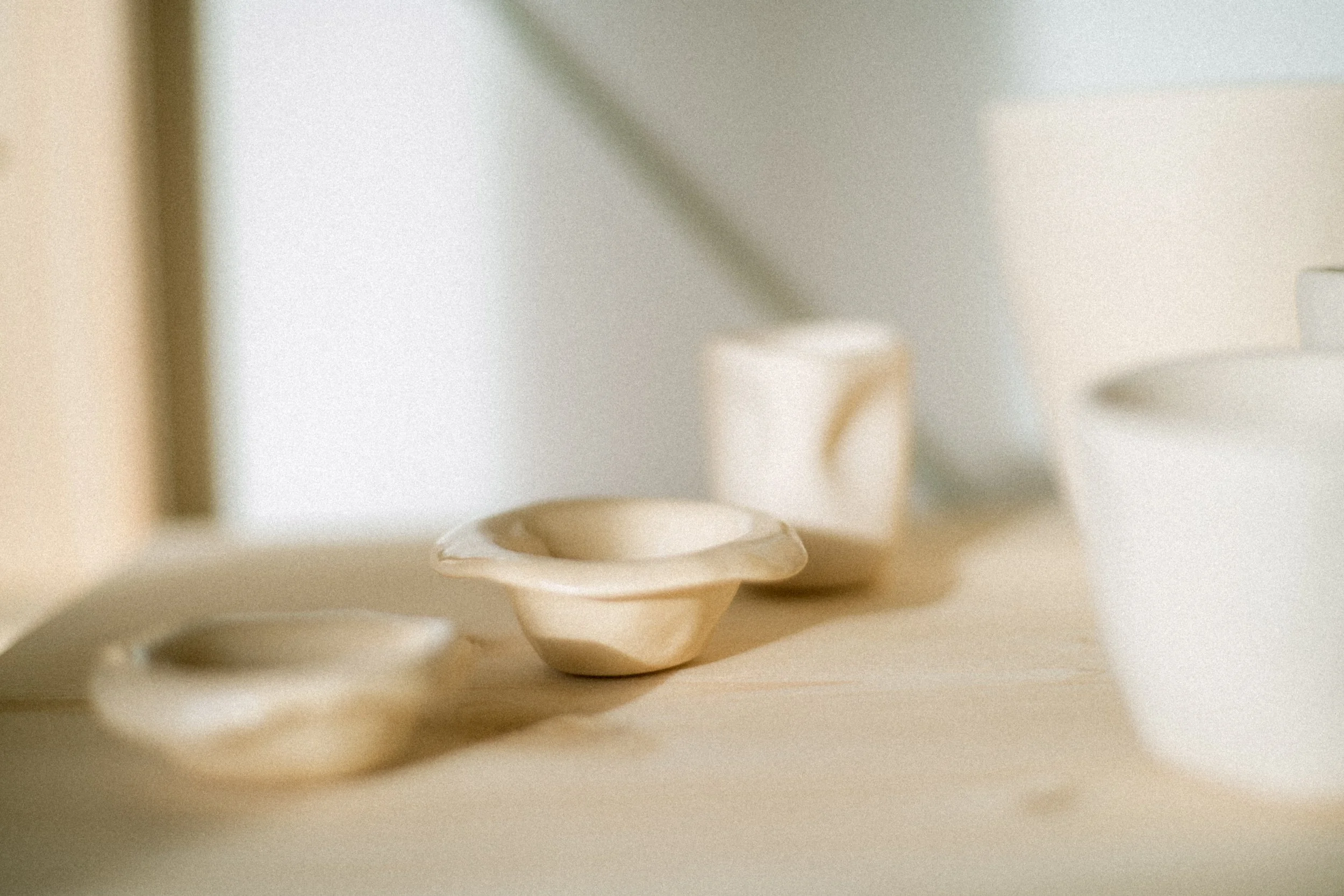 Minimalist ceramic mugs and bowls on a light-colored table with soft natural lighting.