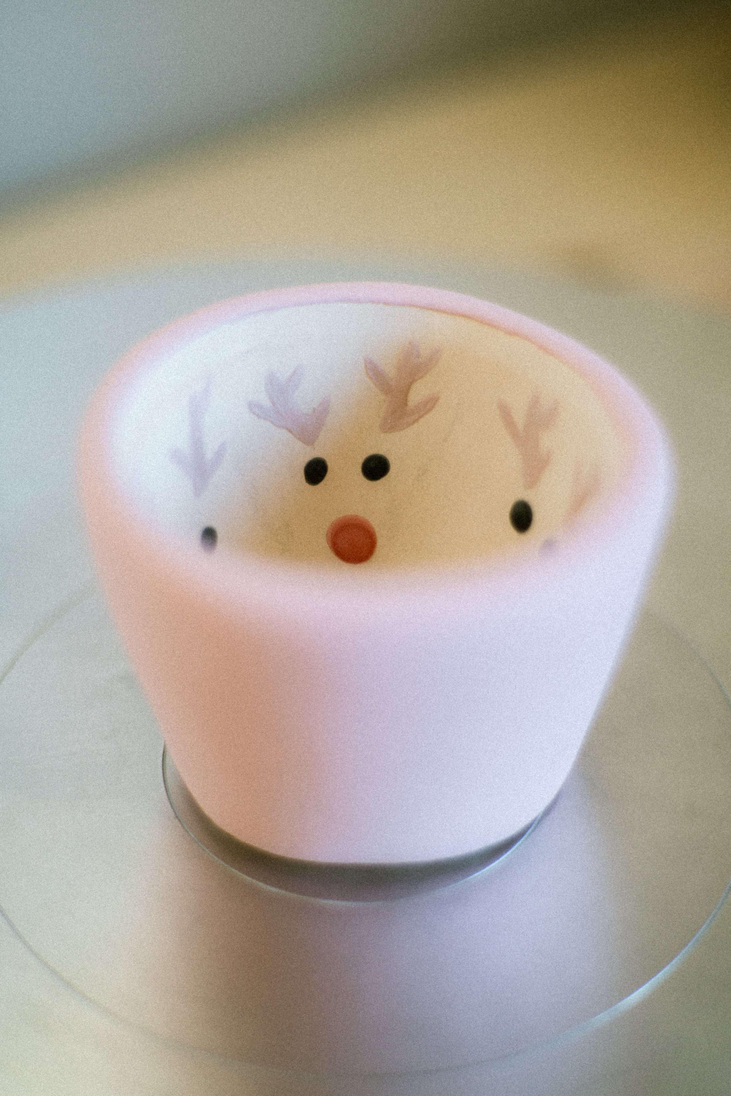 Red mug with a reindeer face design, including black eyes, a red nose, and antlers inside the mug.