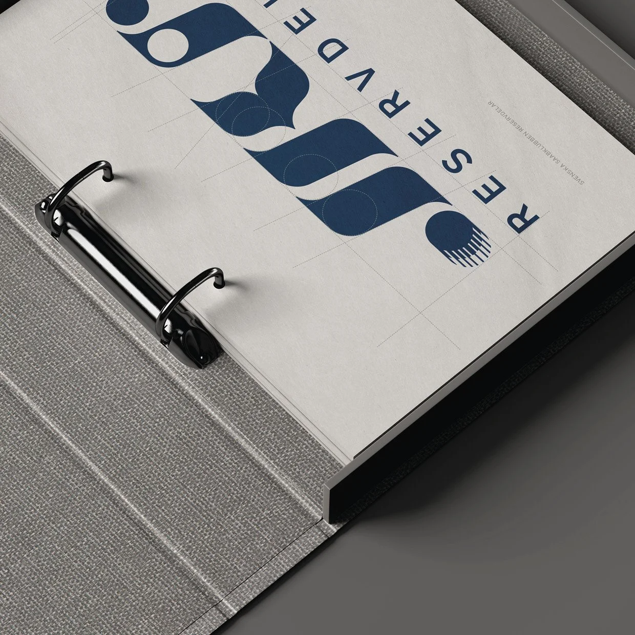 Close-up of a binder with a sheet of paper displaying a geometric logo and the text 'RESERVE DESIGN' in blue. The paper is on a textured gray surface.