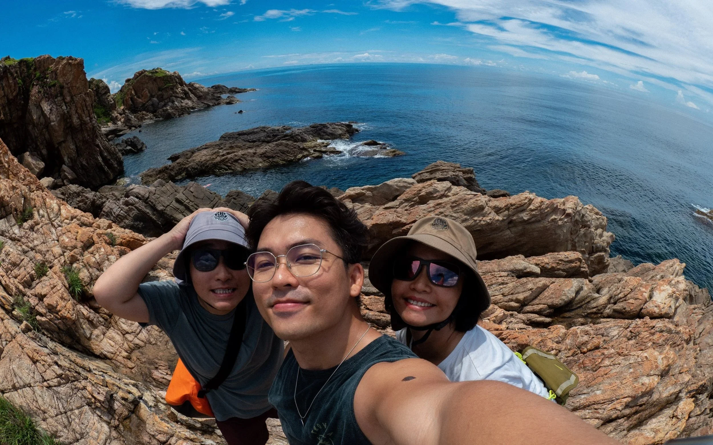 Three friends taking a selfie on rocky coast with the ocean and sky in the background.
