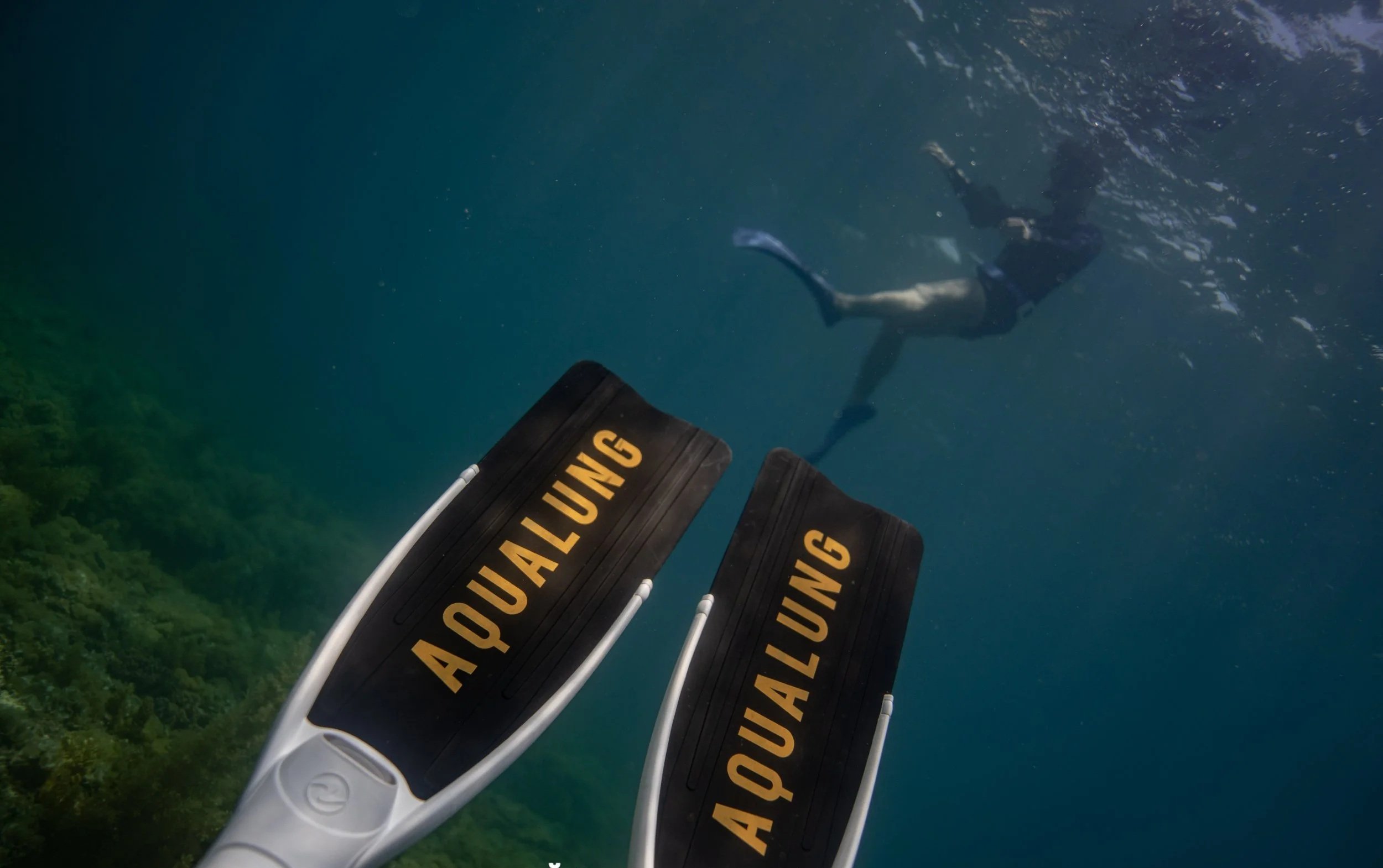 View of a person swimming underwater with fins labeled 'Aqua Lung'
