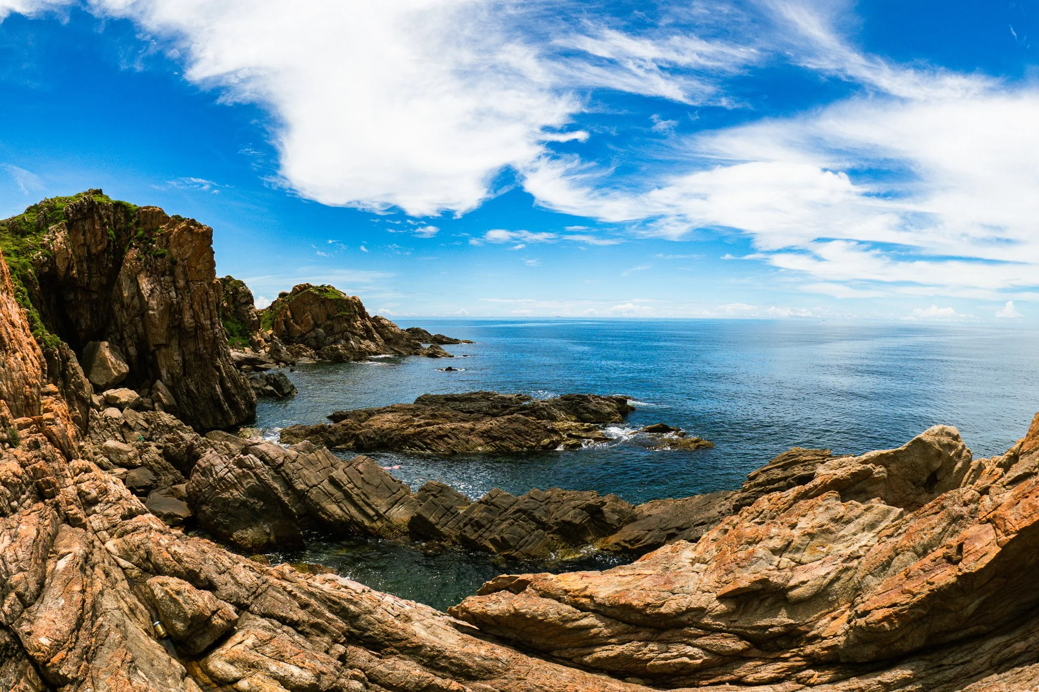 Rocky coastline with cliffs, ocean, and a partly cloudy sky on a sunny day.