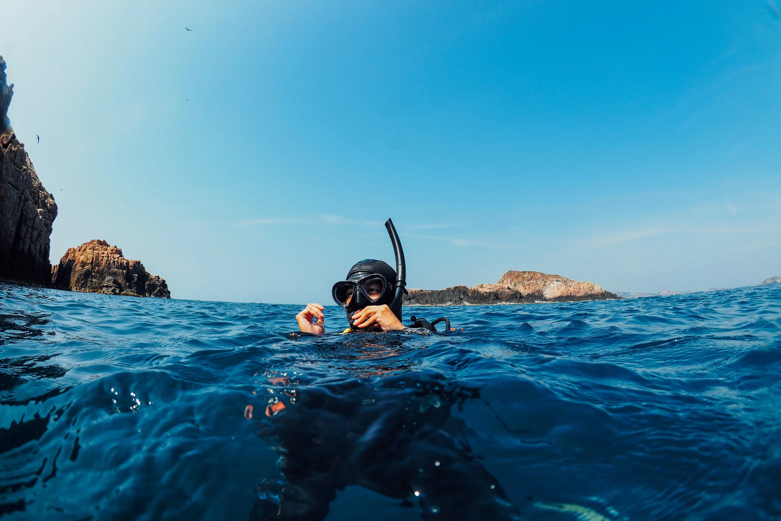 Person snorkeling in the ocean near rocky islands on a clear day.