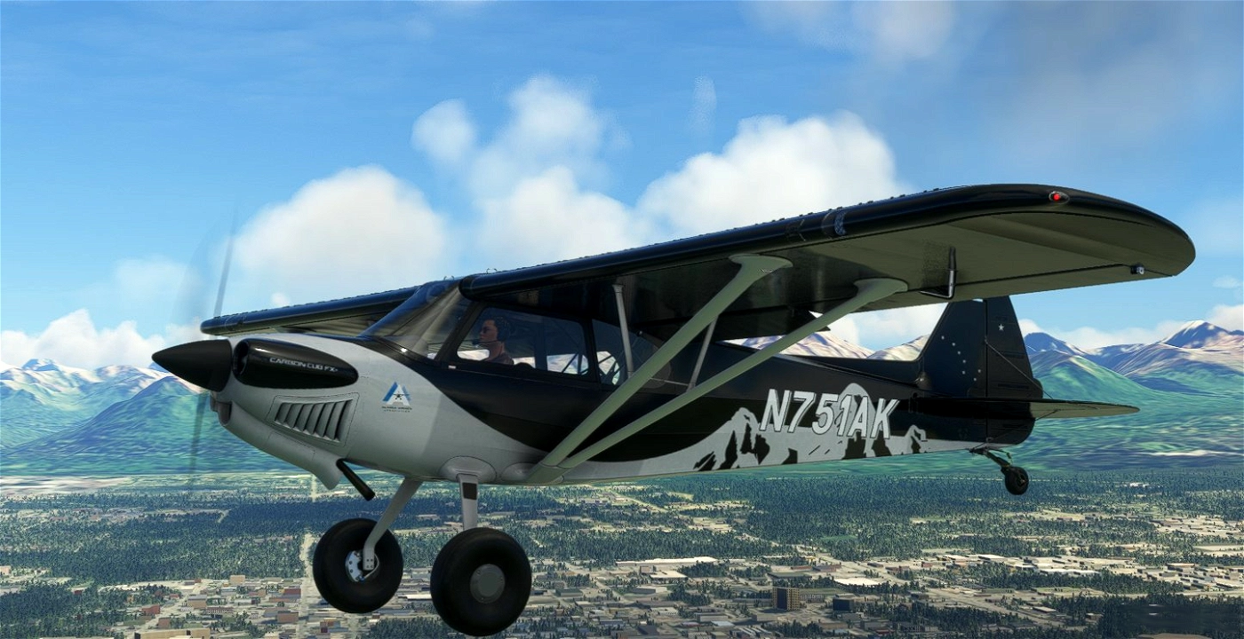 A small black and silver airplane flying above a city with mountains in the background.