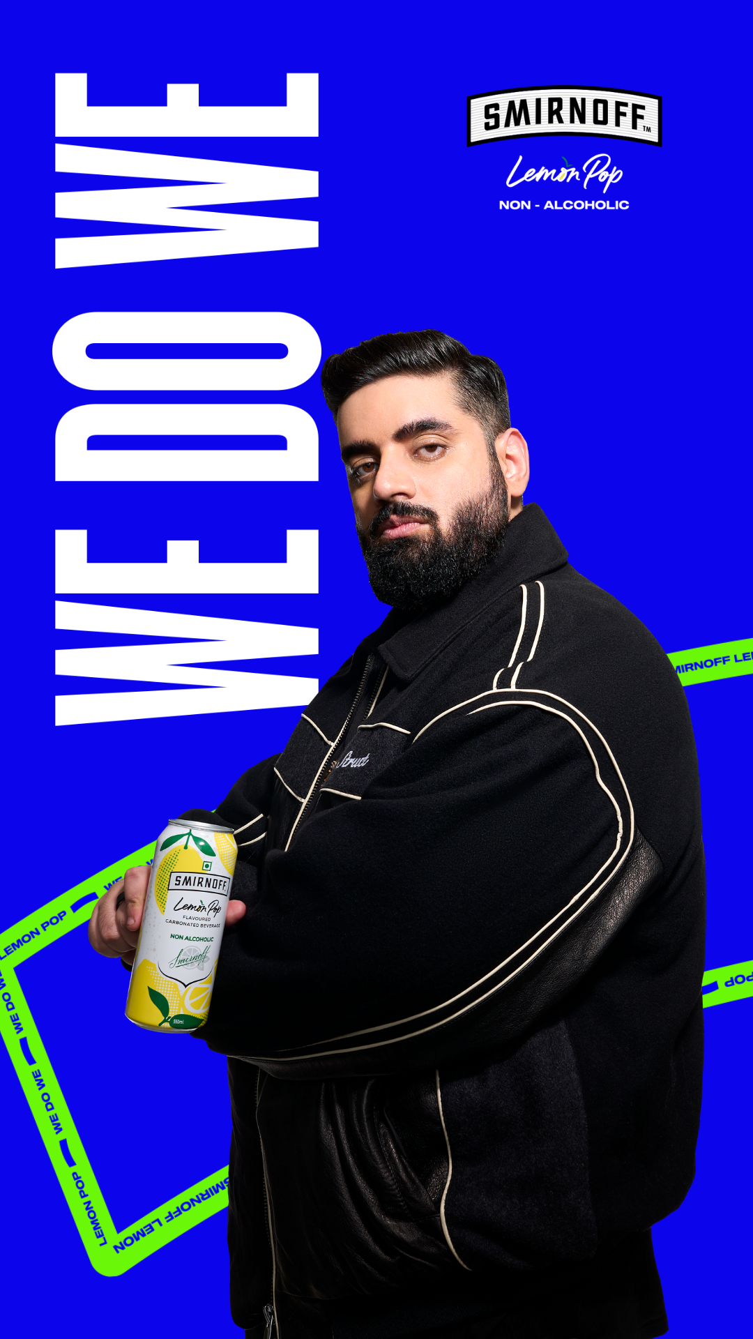 A man with a beard and dark hair holding a tin of Smirnoff Lemon Pop non-alcoholic beverage, standing in front of a blue background with white and green text.