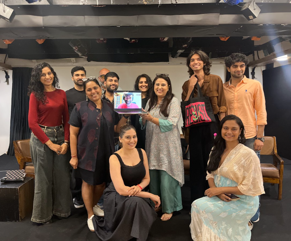 Group of ten people posing together indoors, with one person on a laptop showing on a screen held by a woman, for a film screening.