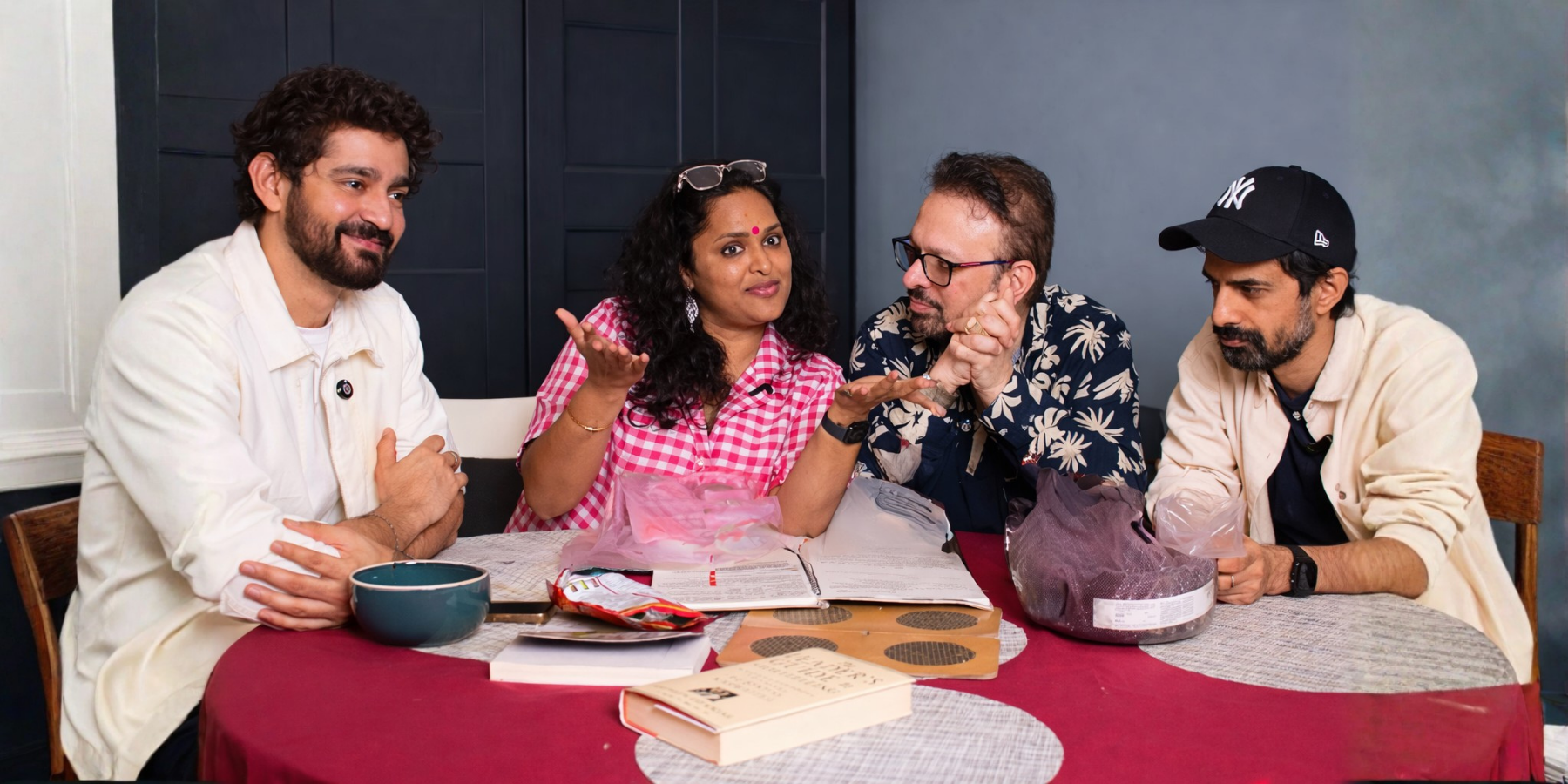 Four people sitting at a table engaged in conversation, with various books and snacks in front of them.
