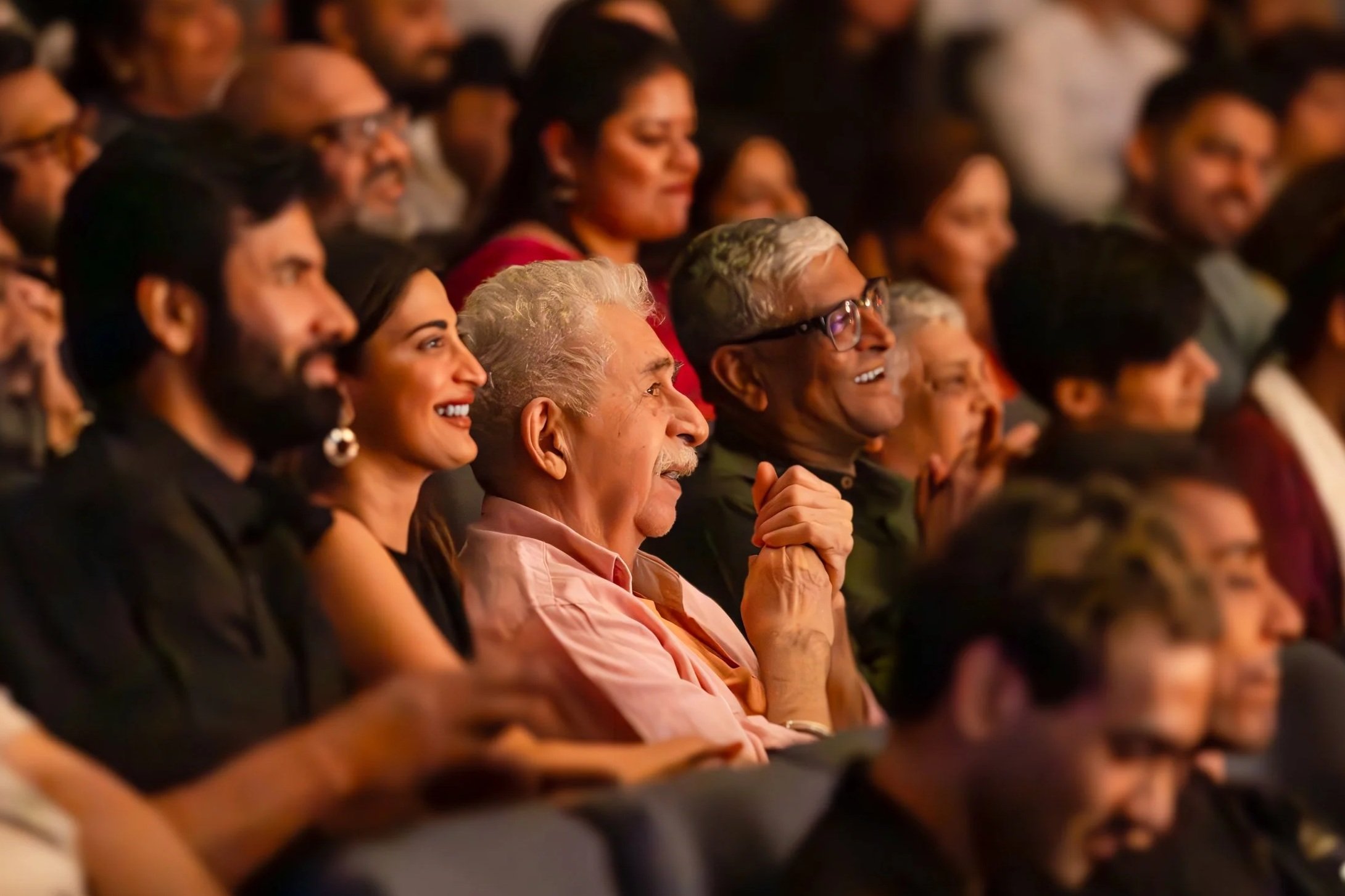 Audience at an event, smiling and enjoying the presentation in a dimly lit theater or auditorium.