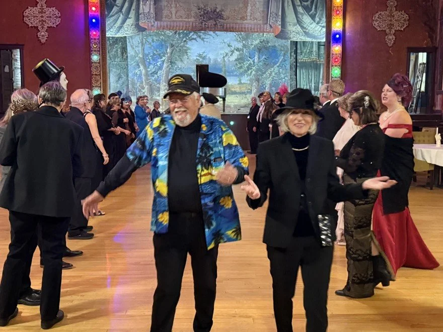 Detectives dancing at a celebration or party in a decorated hall with a large screen and colorful lights.