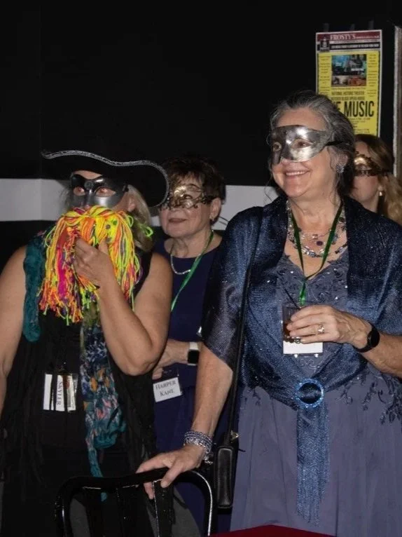 Skyler Peeks is dressed as a pirate in a colorful beard while other masquerade guests wear masks and costumes at the masquerade event.