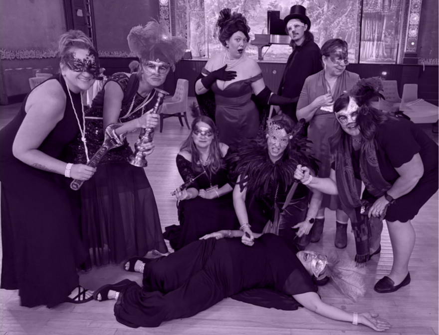 The Murder Mystryss and Phantom of the Batcher Block Opera House among a group of costumed guests posing with fake weapons around another guest pretending to be the victim.