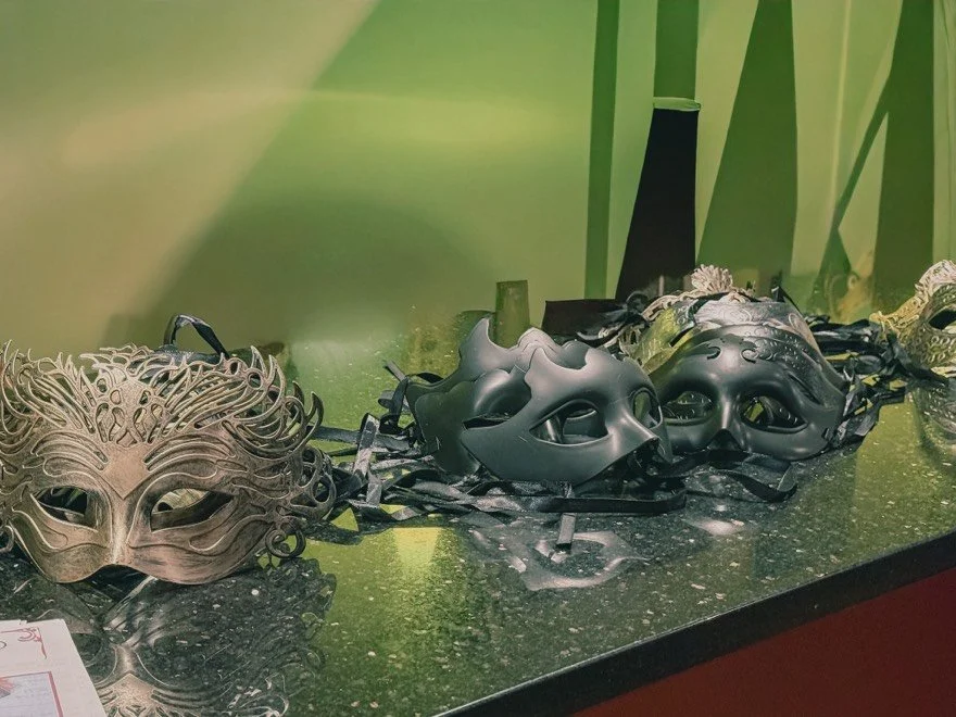 A display of decorative masquerade masks on a black tabletop with a green and natural-themed background.