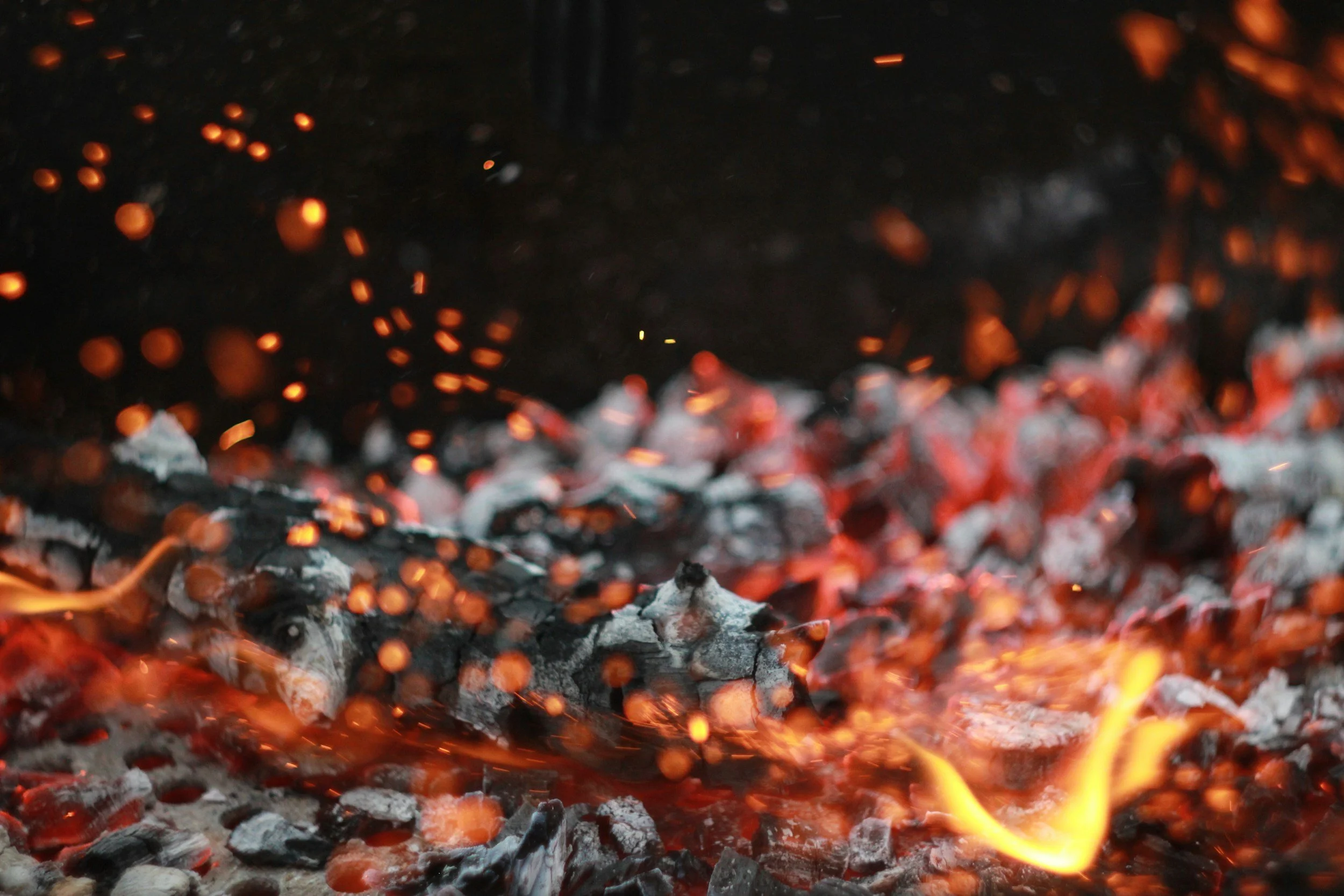 Close-up of hot glowing charcoal embers and small flickering flames.