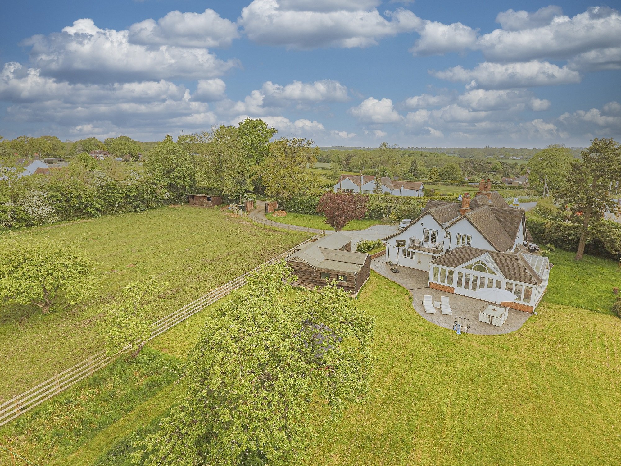 Aerial view of a white house with a large backyard, trees, and a surrounding fence on a partly cloudy day.