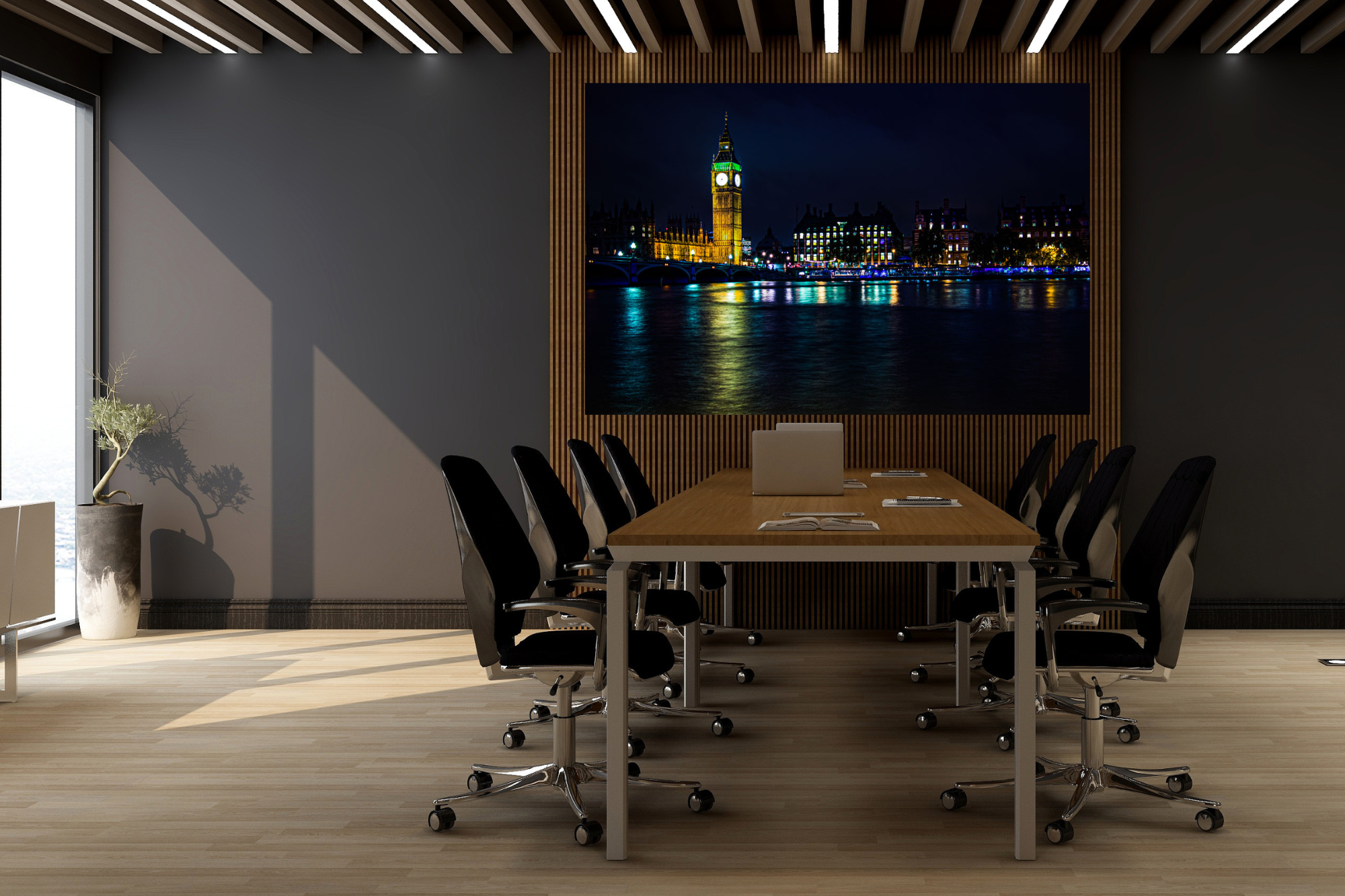 Modern conference room with a large wooden table surrounded by black office chairs, a laptop, notebooks, and a pen on the table. A large nighttime photo of Big Ben and the Houses of Parliament in London is displayed on the wall. There is a potted pla