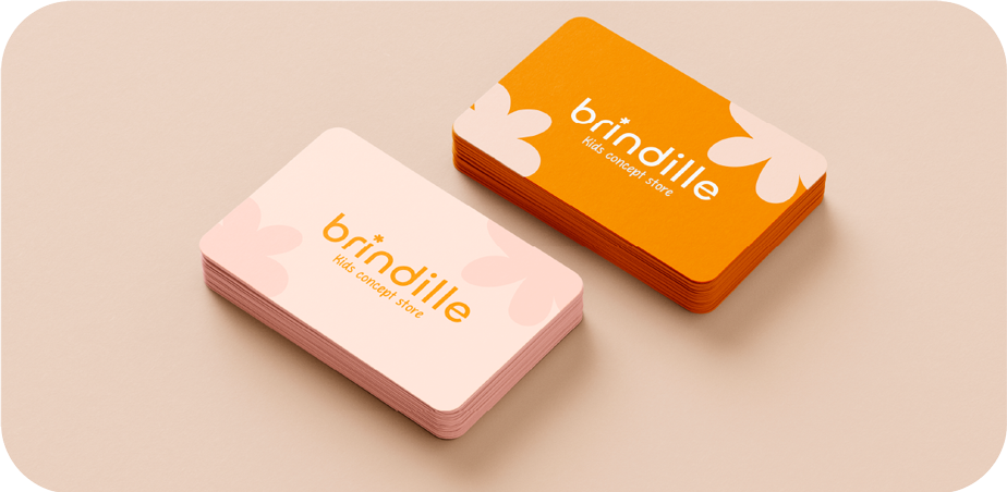 Deux paquets de cartes de visite pour une boutique de jouets nommée 'brindille', avec un design coloré et floral, une couleur de fond rose pour l'une et orange pour l'autre.